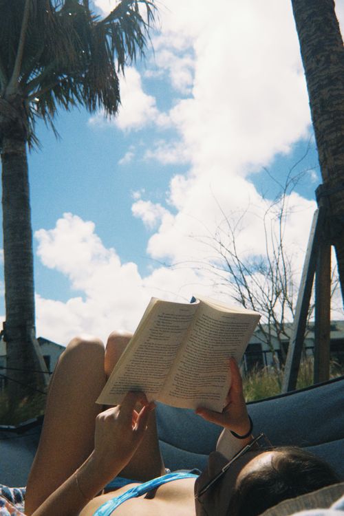 Free Woman enjoying a book while relaxing in a hammock under palm trees on a sunny day. Stock Photo