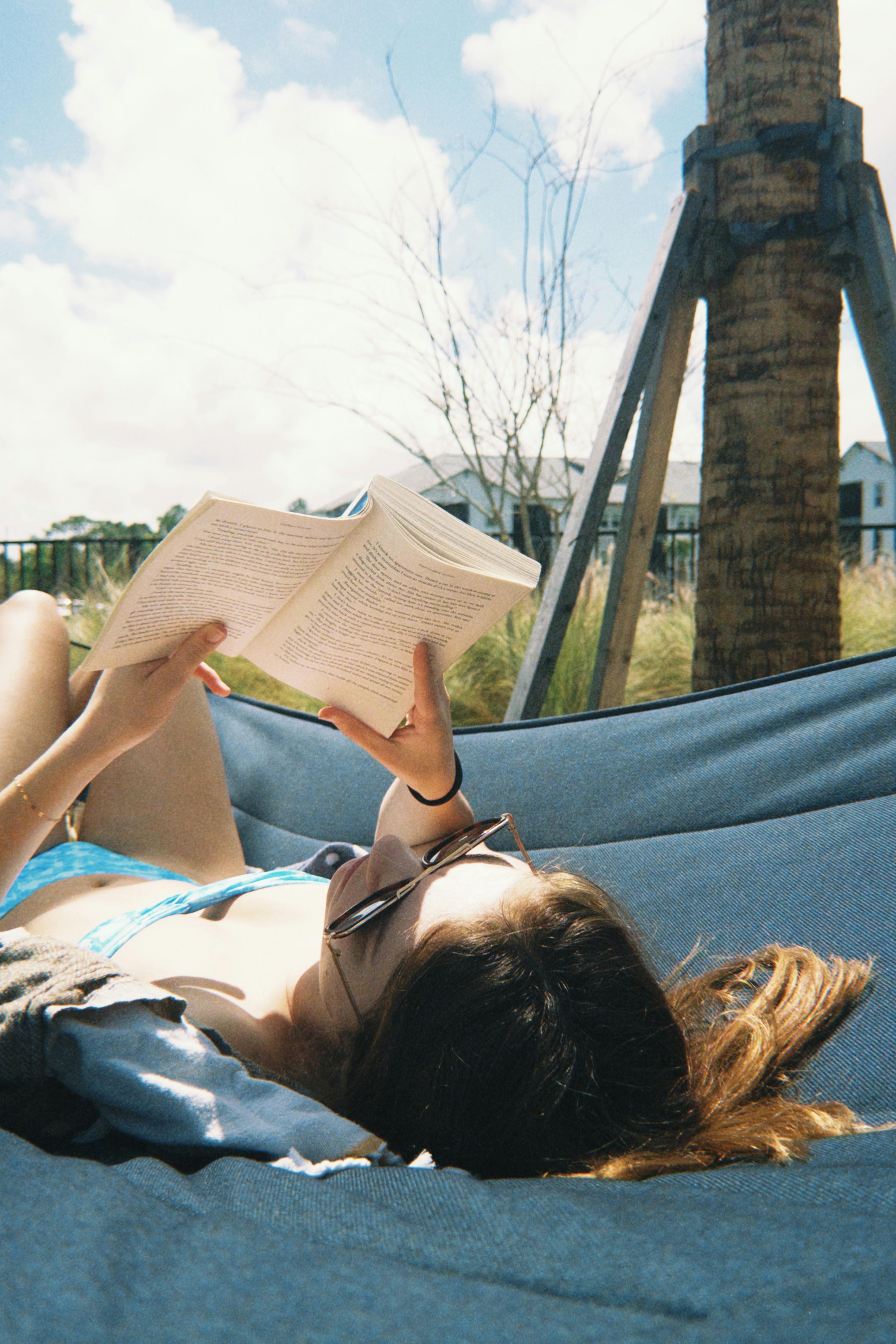 Zadarmo Mladá žena číta v hojdacej sieti za slnečného dňa a užíva si voľný čas vonku. Fotka z fotobanky