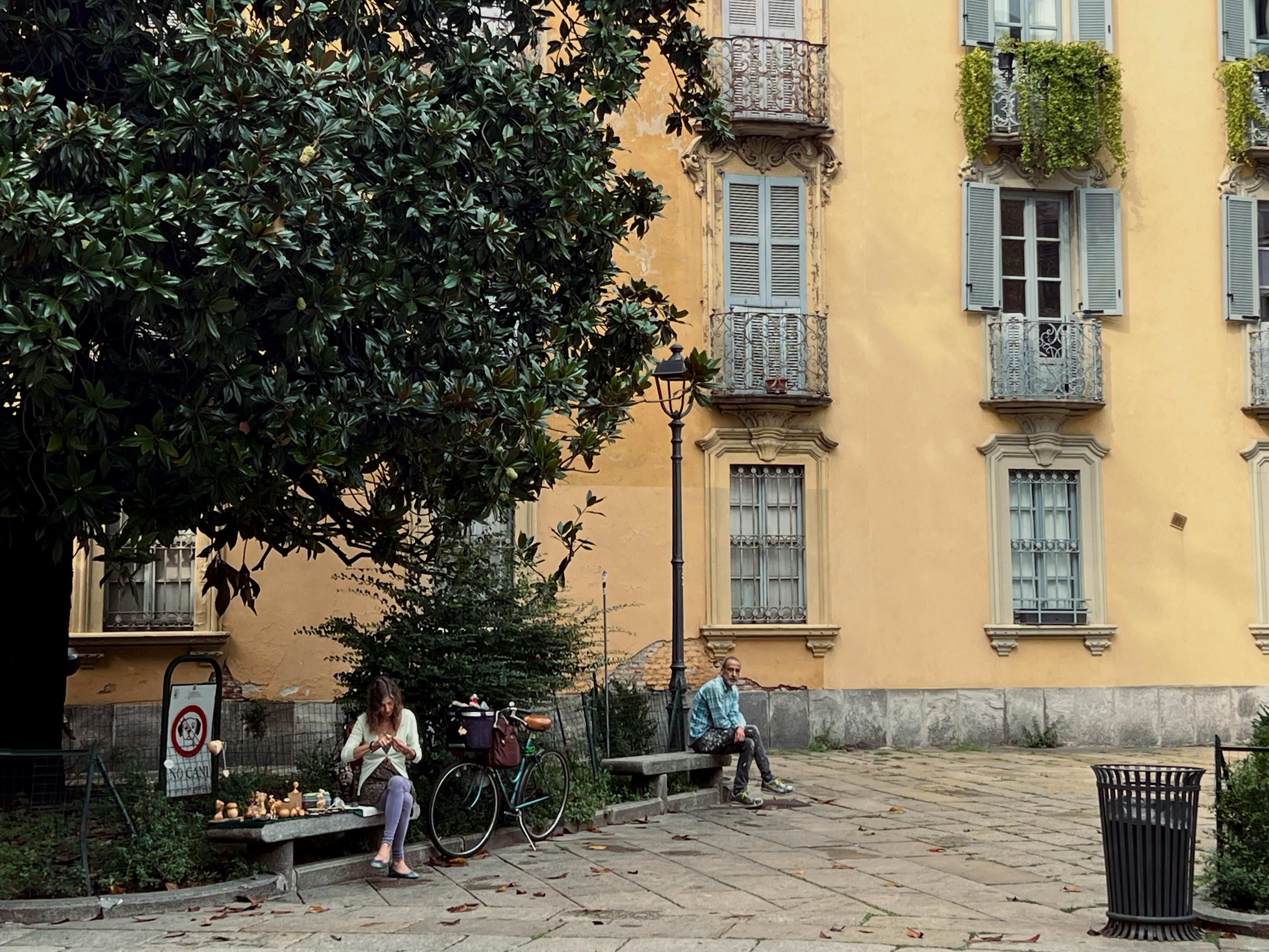 Gratuit Deux personnes se détendent sur des bancs dans une charmante place européenne à l'architecture vibrante. Photos
