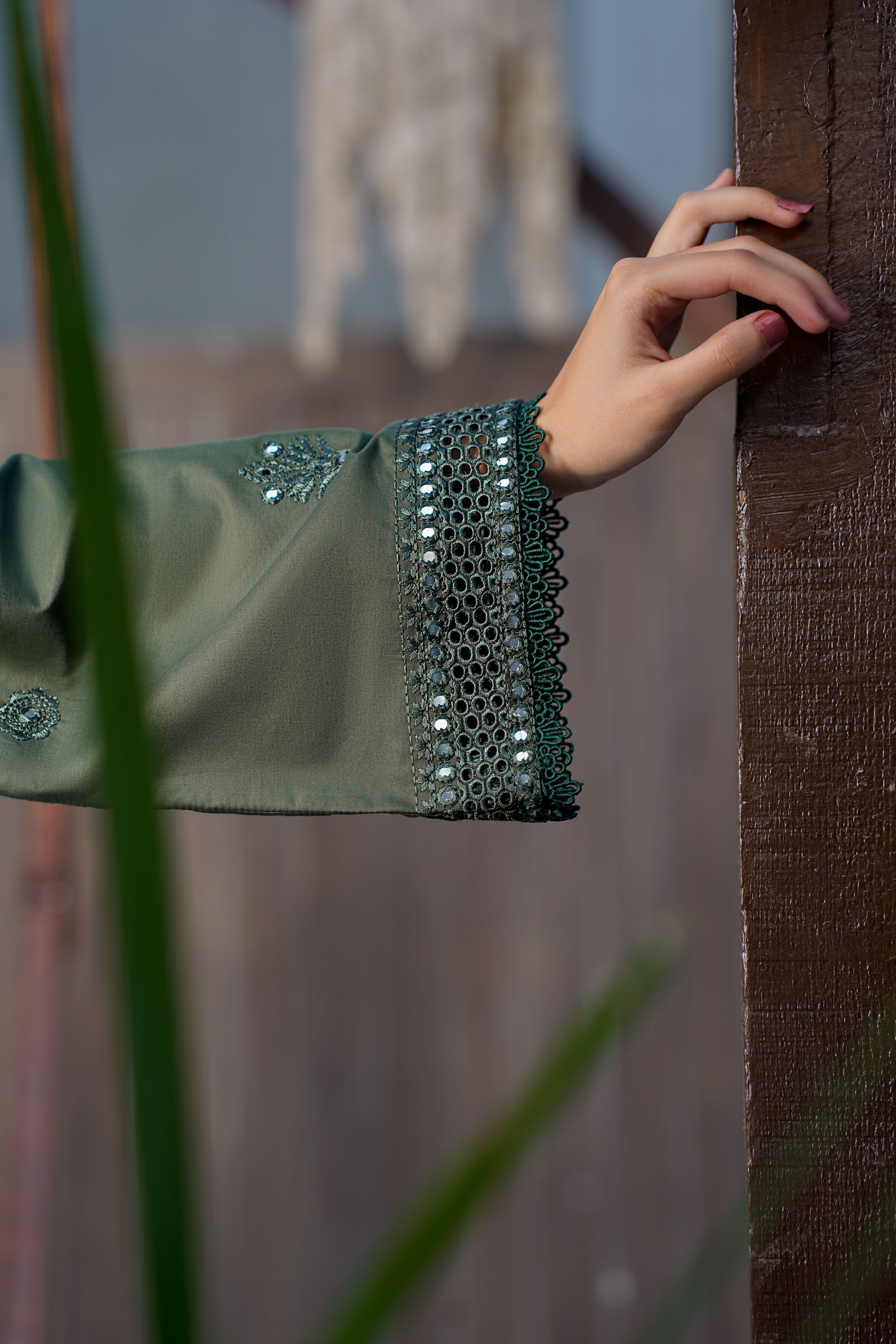 Close-up of a hand in a green embroidered sleeve against a wooden backdrop, showcasing Eastern fashion.
