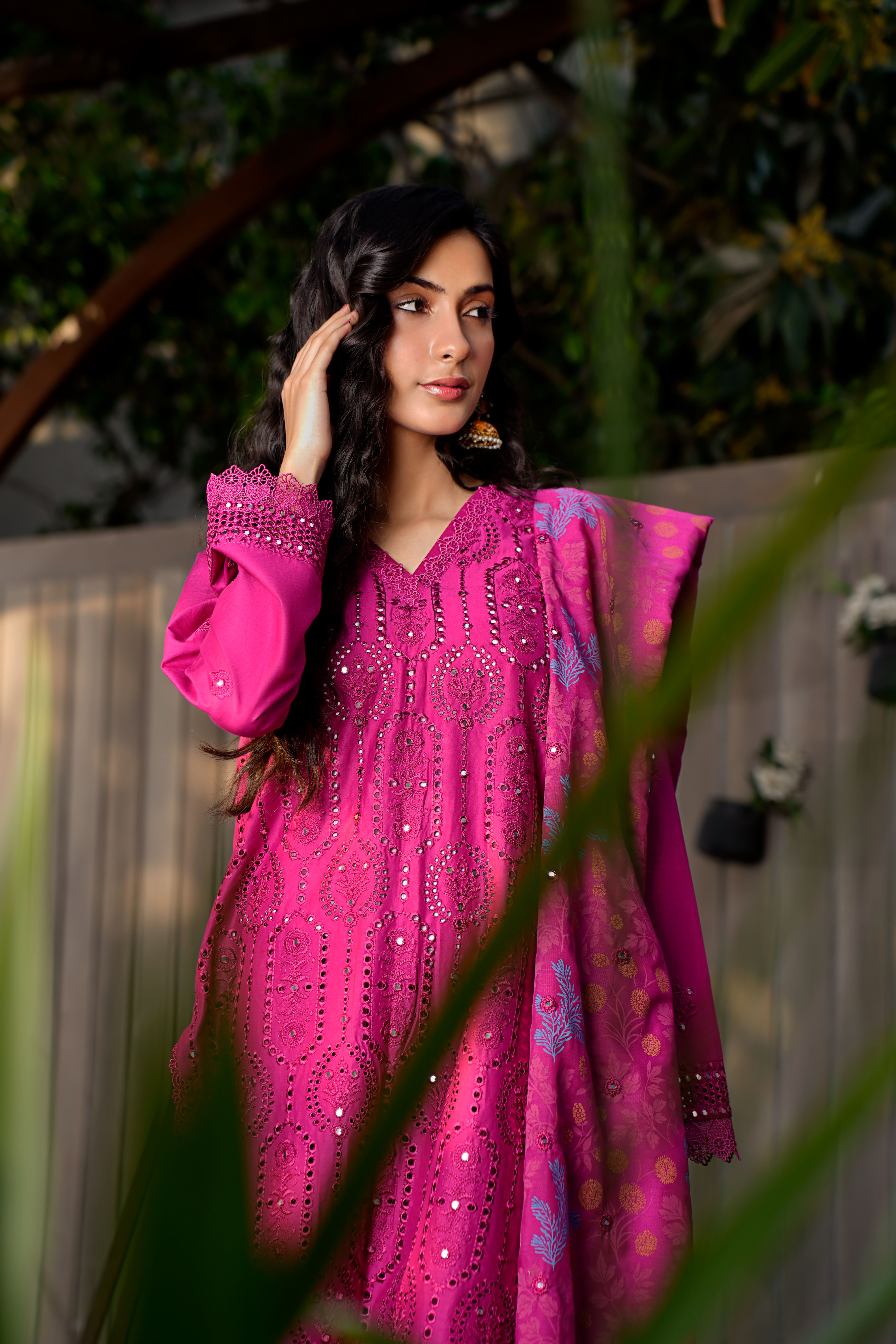 Portrait of a woman in a pink embroidered dress in a garden setting, showcasing fashion and style.