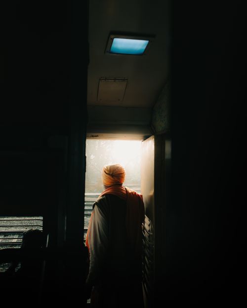 Free A person enjoys a peaceful morning view from a train doorway in India, basking in sunlight. Stock Photo