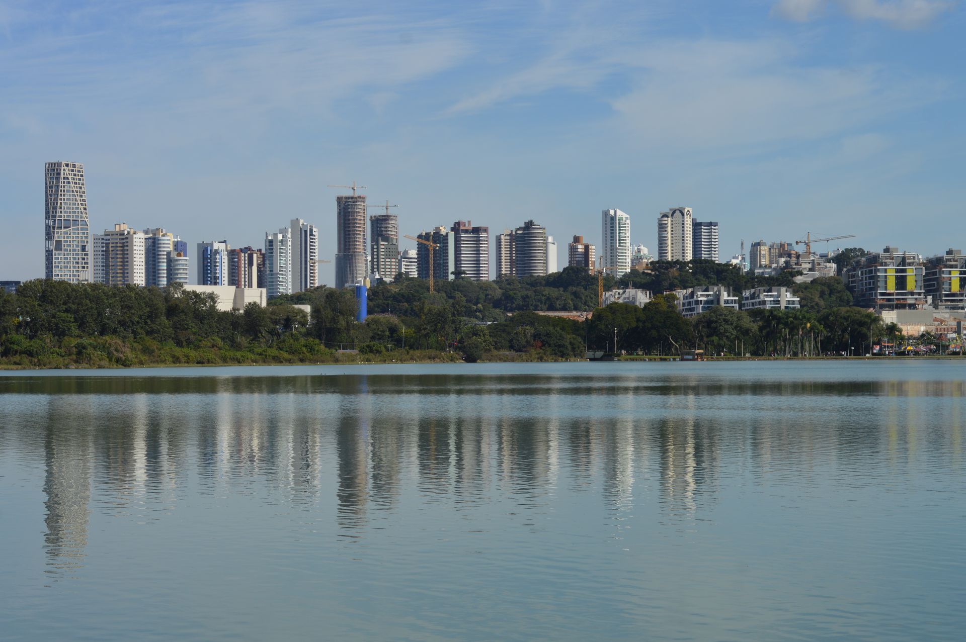 Skyline of Curitiba, Brazil, reflecting on a serene lake under a clear blue sky.