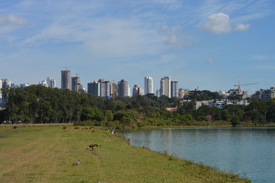 Cityscape of Curitiba with high-rise buildings and park lake under a clear sky.