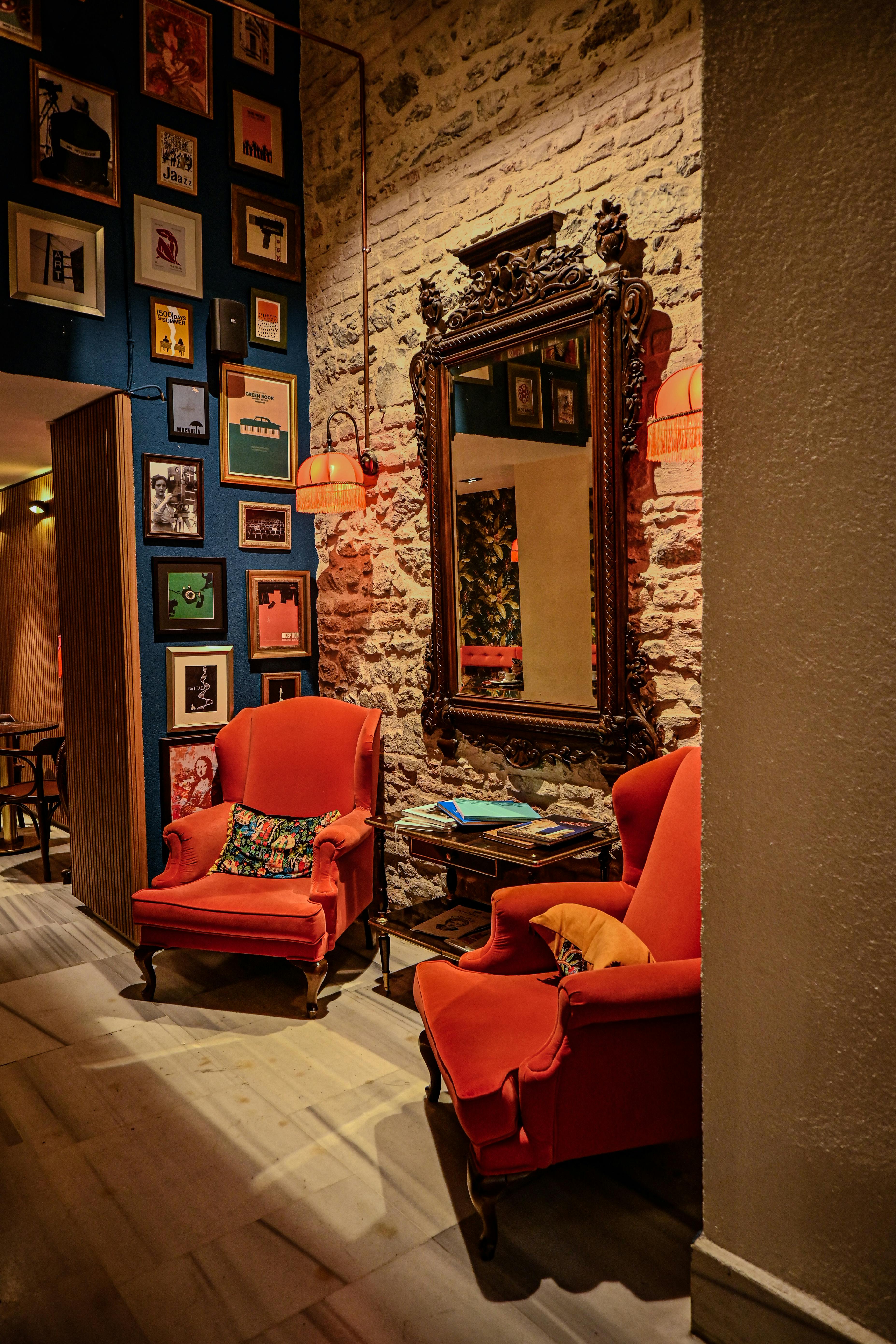 Gratis Accogliente salotto in stile vintage con poltrone rosse, specchio decorato e opere d'arte eclettiche alle pareti. Foto a disposizione