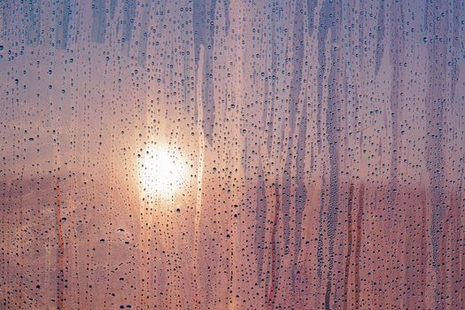 Beautiful sunset seen through a window with raindrops, creating a moody atmosphere.