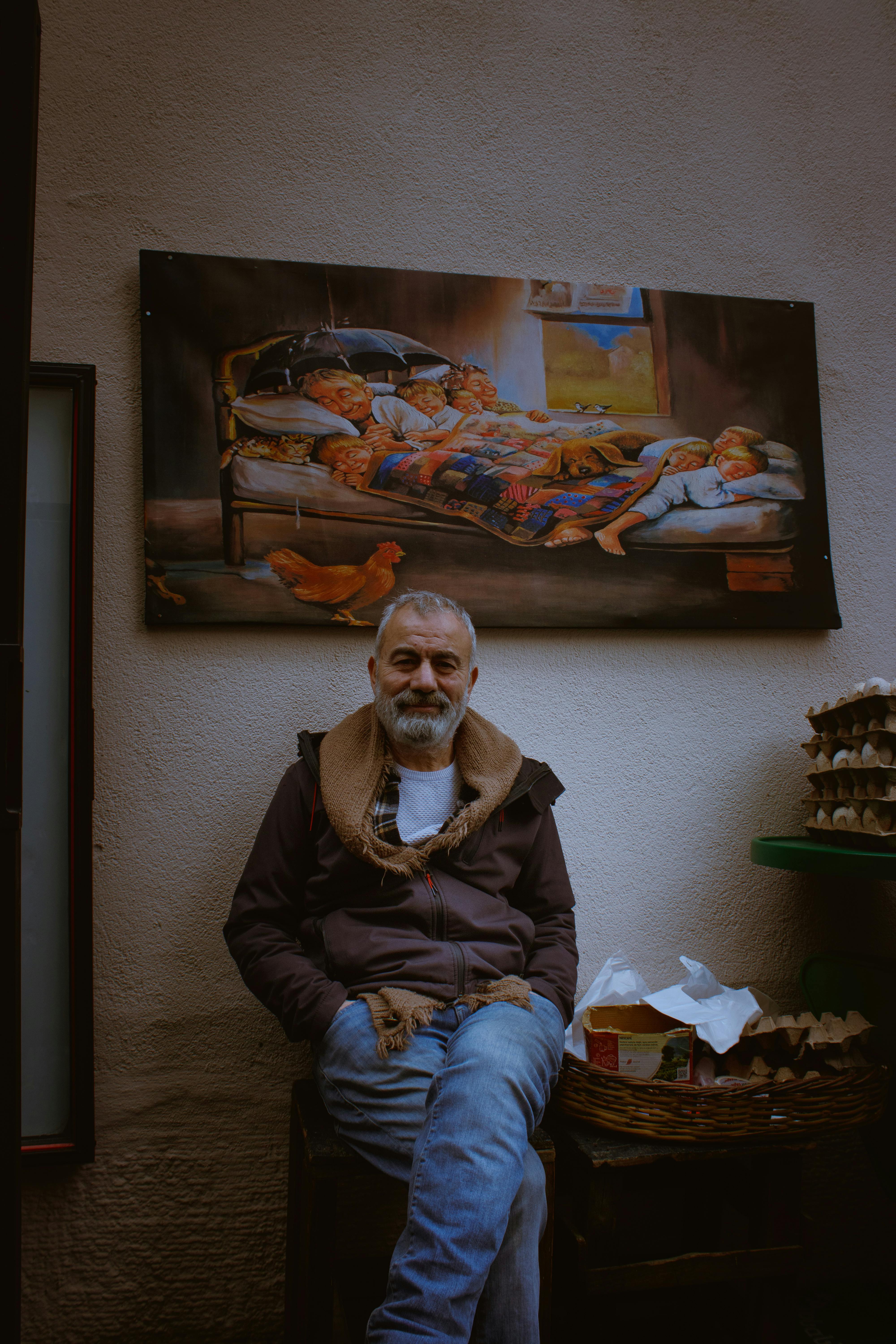 Miễn phí Người đàn ông có râu ngồi trong nhà dưới một bức tranh rực rỡ, toát lên vẻ thư thái và trầm tư. Ảnh lưu trữ