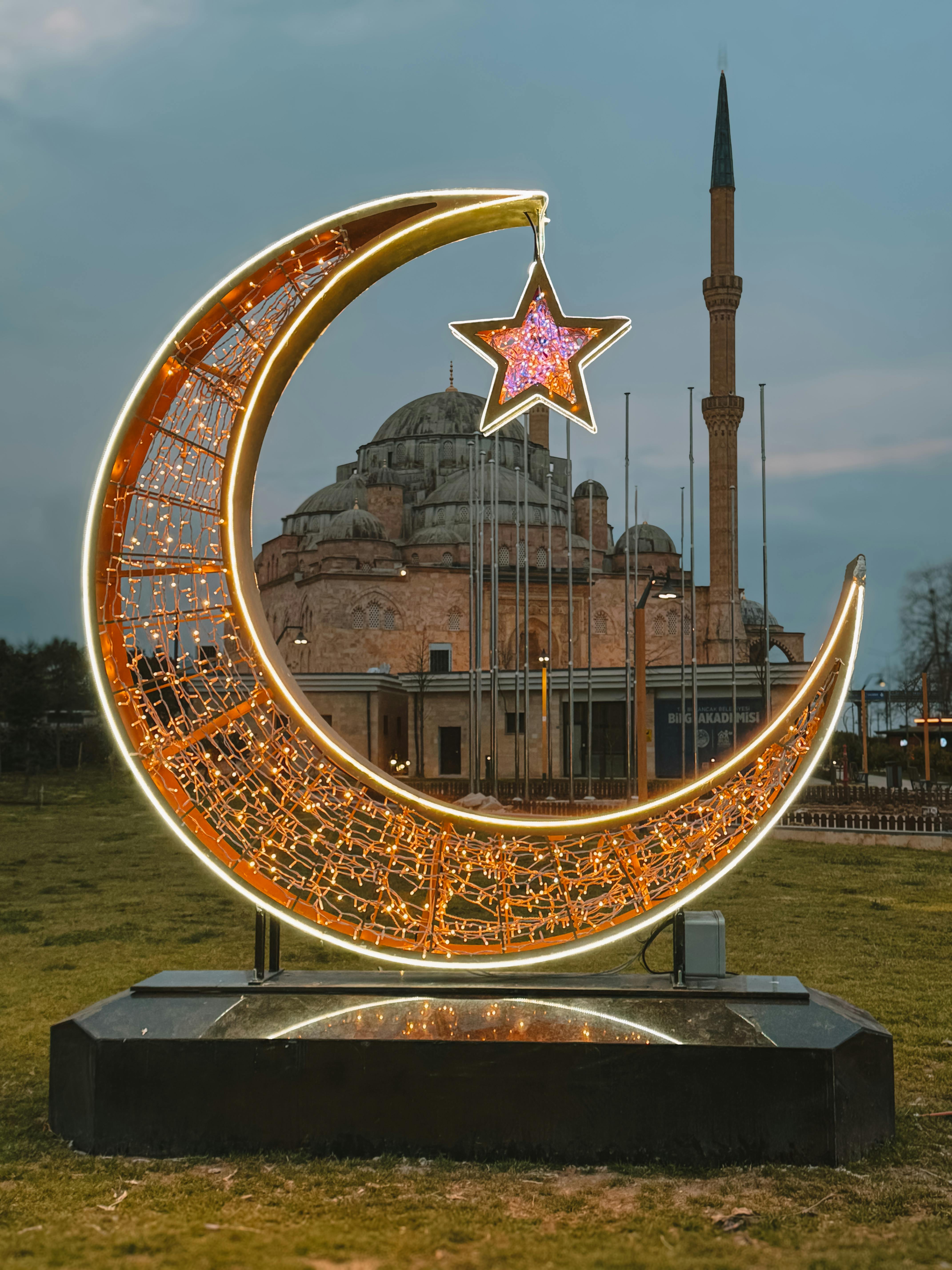 Illuminated crescent and star in front of a historic mosque at dusk in Giresun, Türkiye.