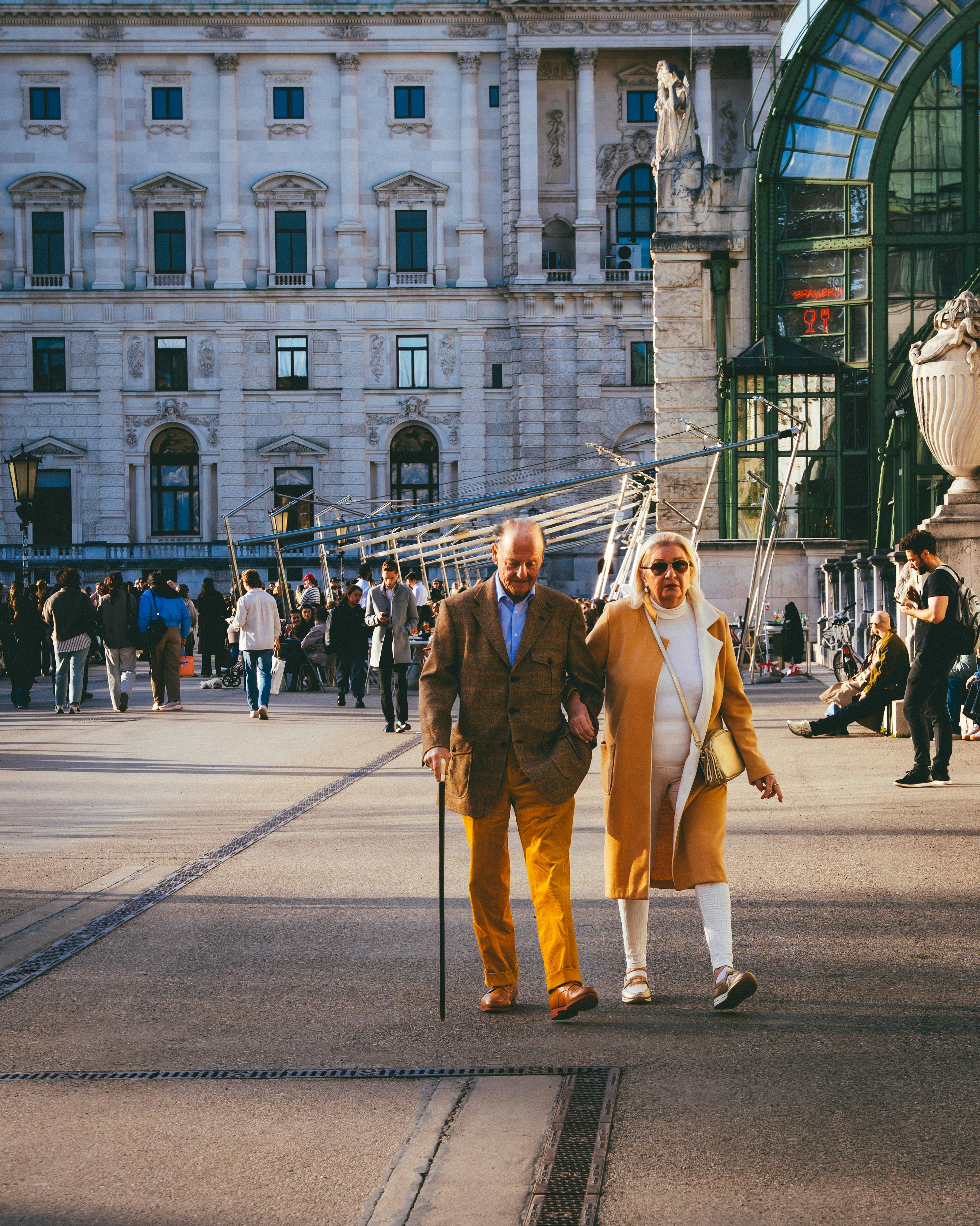 免費 一對老年夫婦在維也納霍夫堡宮散步，享受著陽光明媚的一天，周圍還有許多人。 圖庫相片