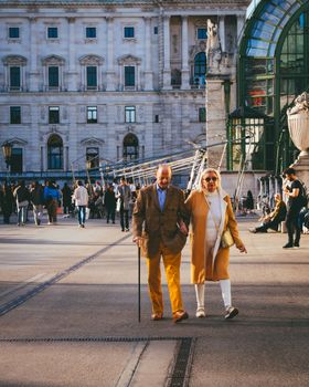 An elderly couple walking at Hofburg Palace, Vienna, enjoying a sunny day with people around.