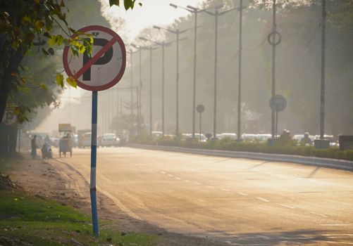 View of a bustling Indian street with a no parking sign, trees, and vehicles in the warm evening light.