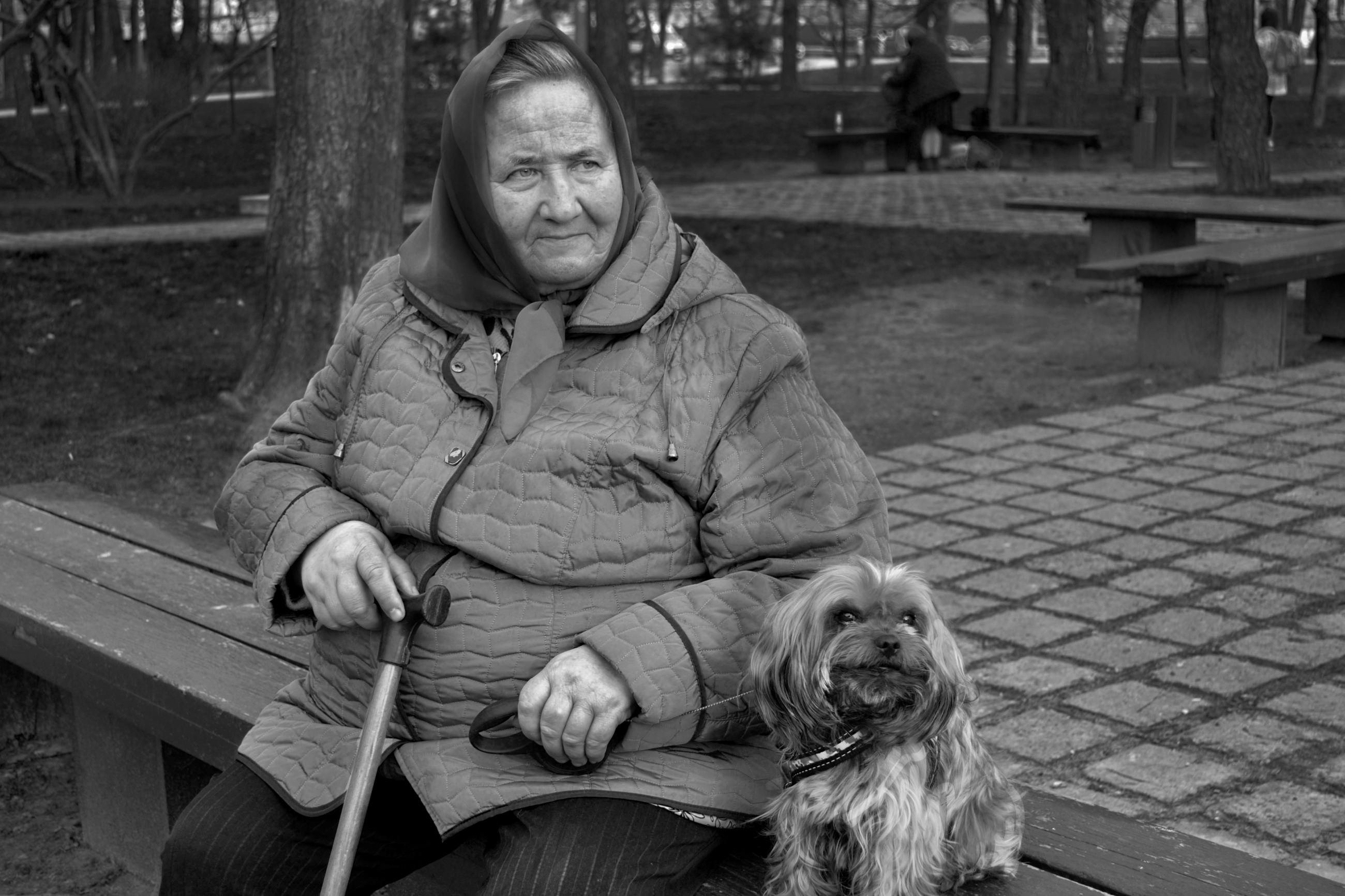 A senior woman sitting on a park bench with her dog in a black and white photograph. 