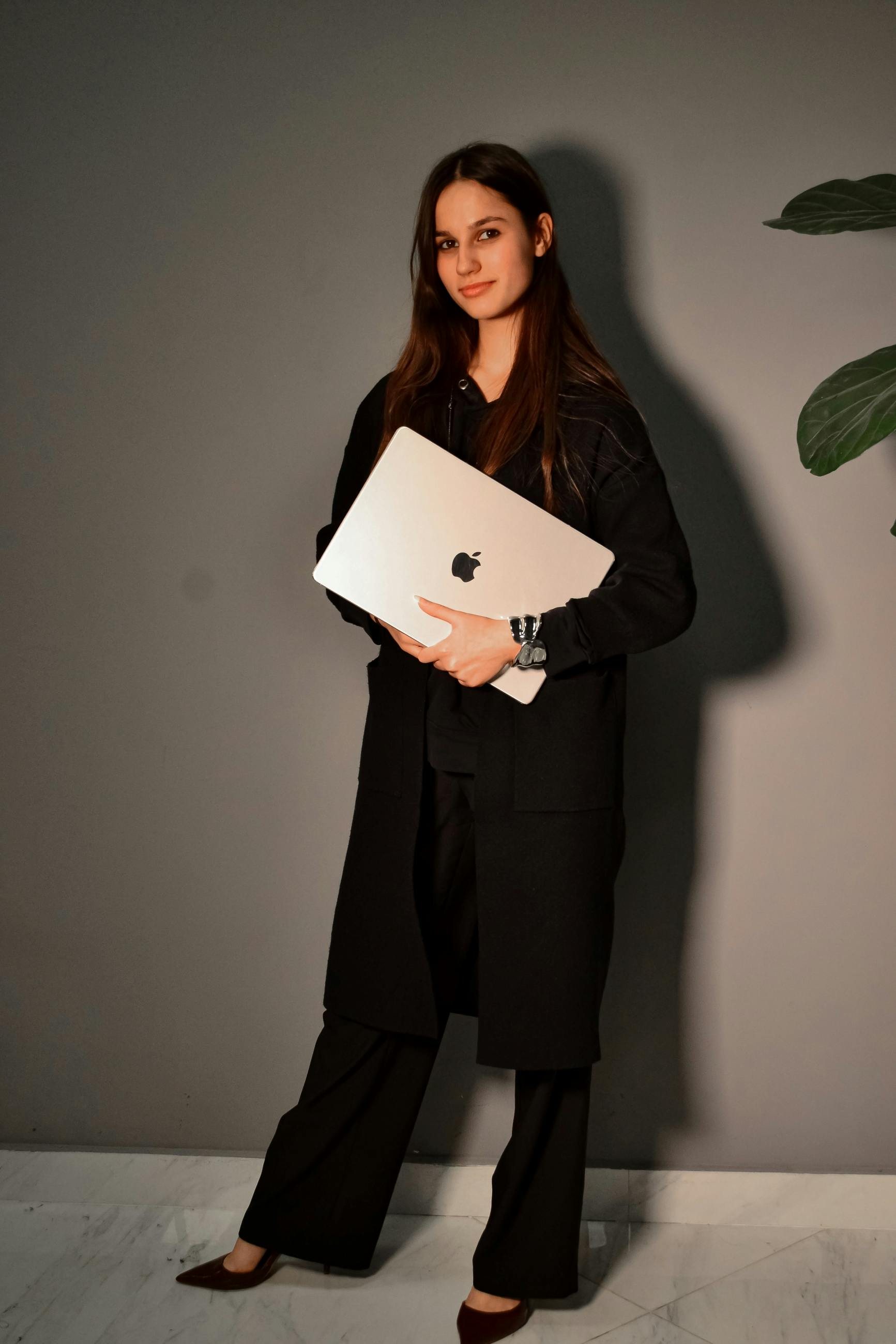 Confident woman in black attire holding a laptop indoors.