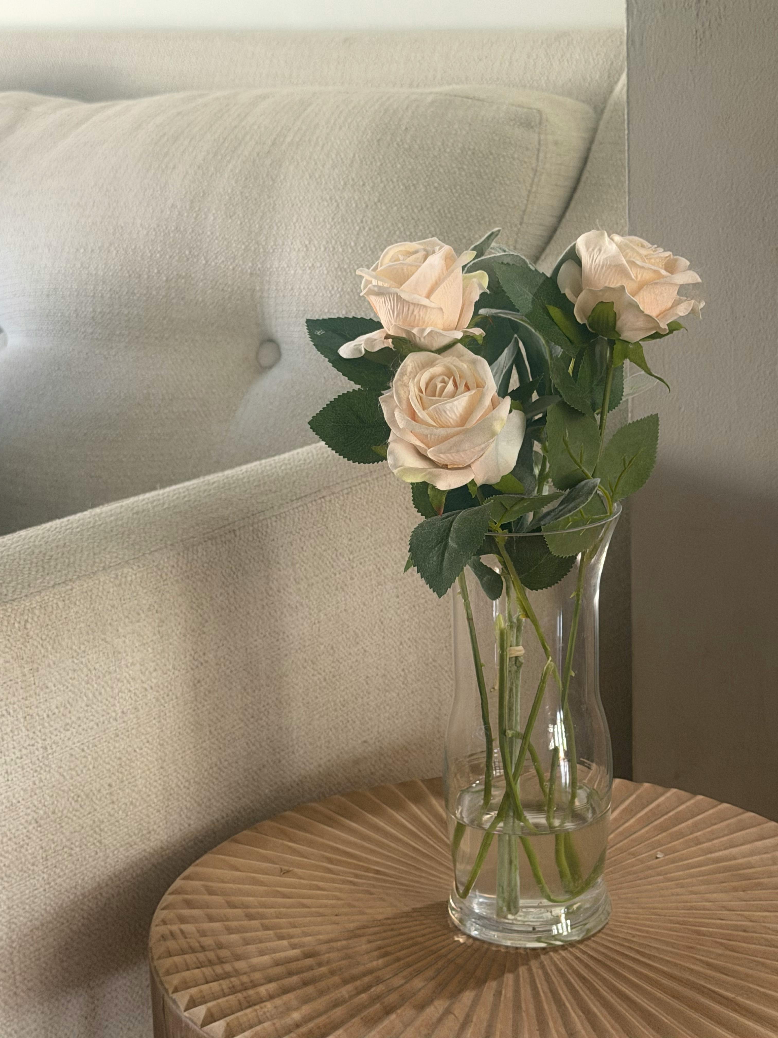 Kostnadsfria Minimalistisk blomsterdekor med vita rosor i en glasvas på ett texturerat träbord. Stock foto