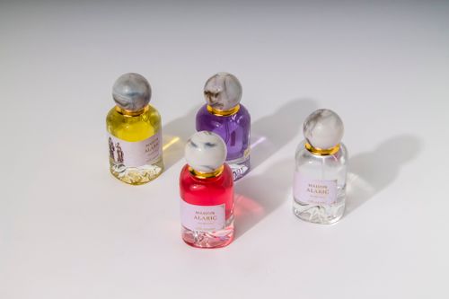 Free Four Maison Alarie perfume bottles with colored liquids on a white surface, casting shadows. Stock Photo