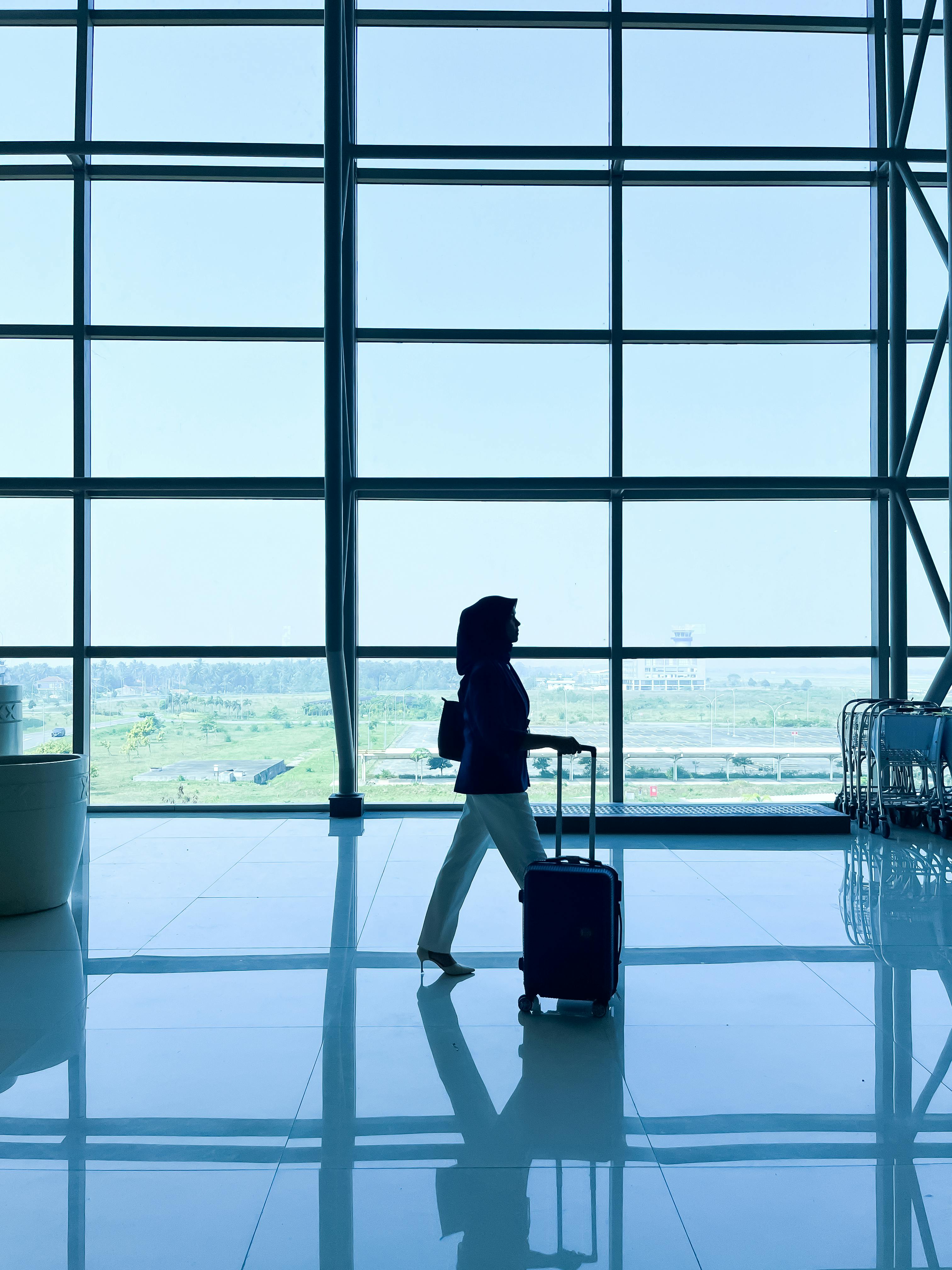 Gratuit Călător singur cu bagaje conturate pe fațada de sticlă a terminalului, surprinzând contemplarea liniștită în timpul tranzitului. Fotografie de stoc