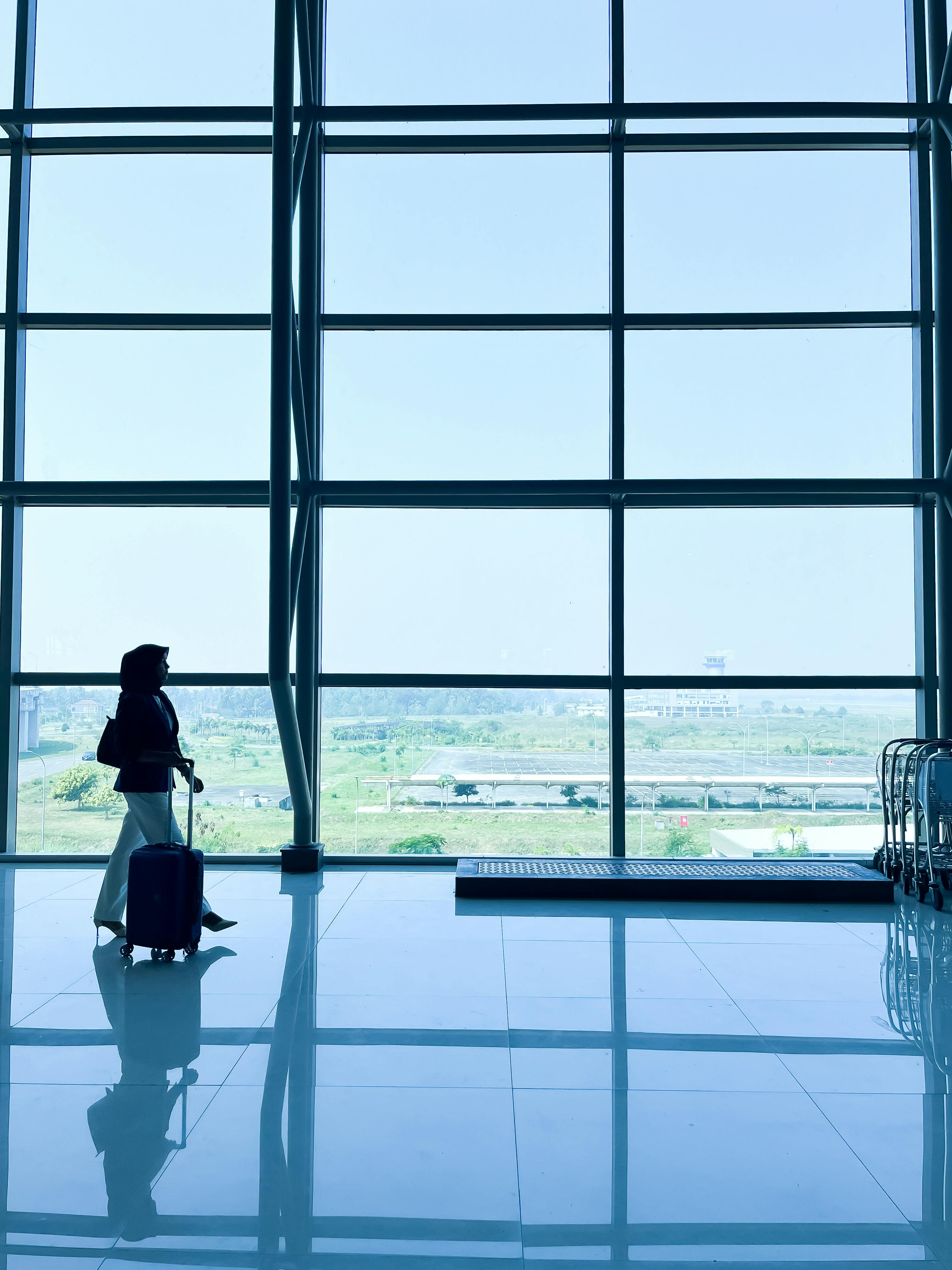 Bezpłatne Sylwetka samotnego podróżnika idącego z bagażem przez nowoczesne lotnisko w Indonezji. Zdjęcie z galerii