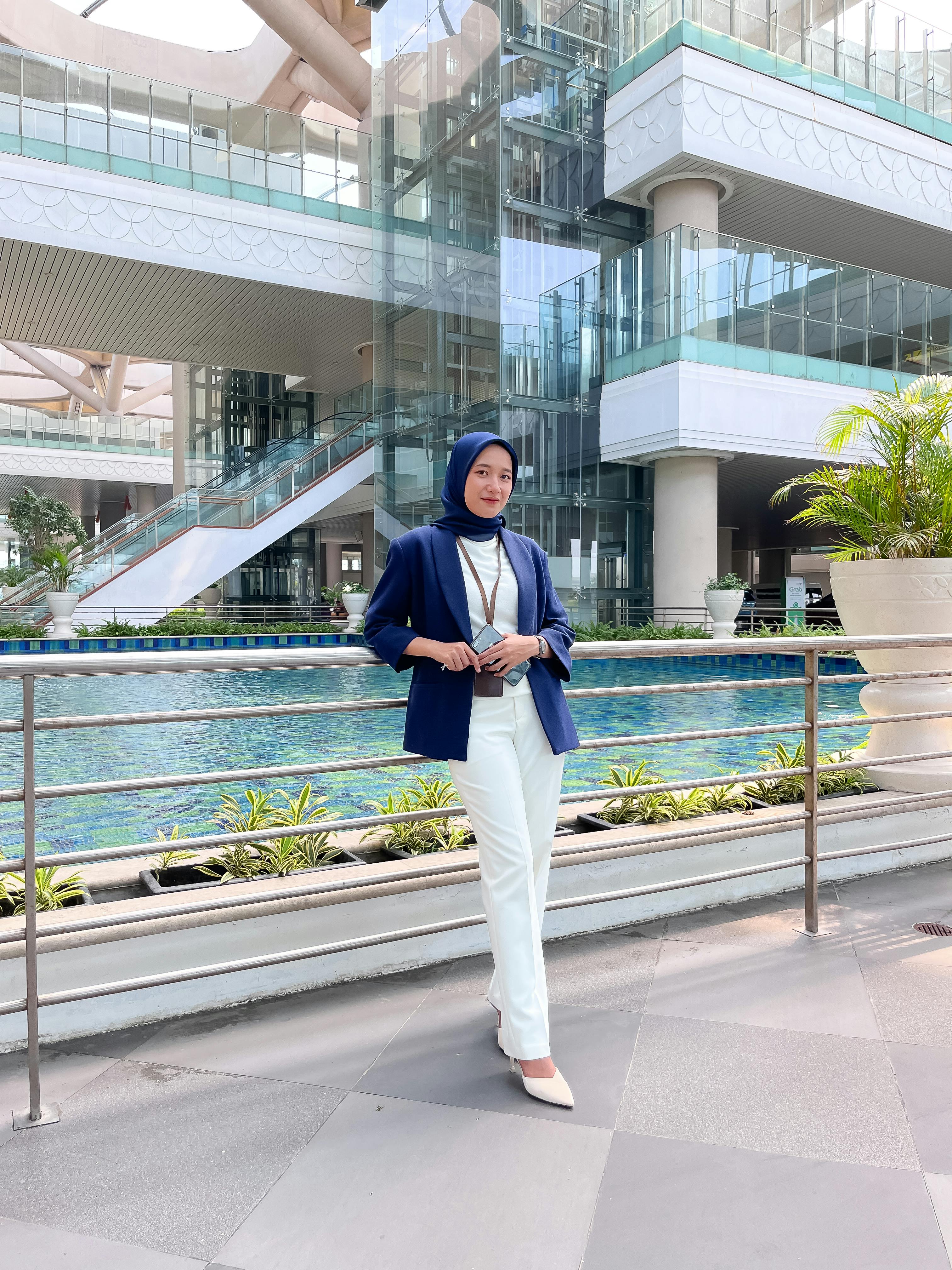 grátis Mulher de negócios confiante, vestida com elegância, em pé em frente a um edifício moderno da arquitetura indonésia. Foto profissional
