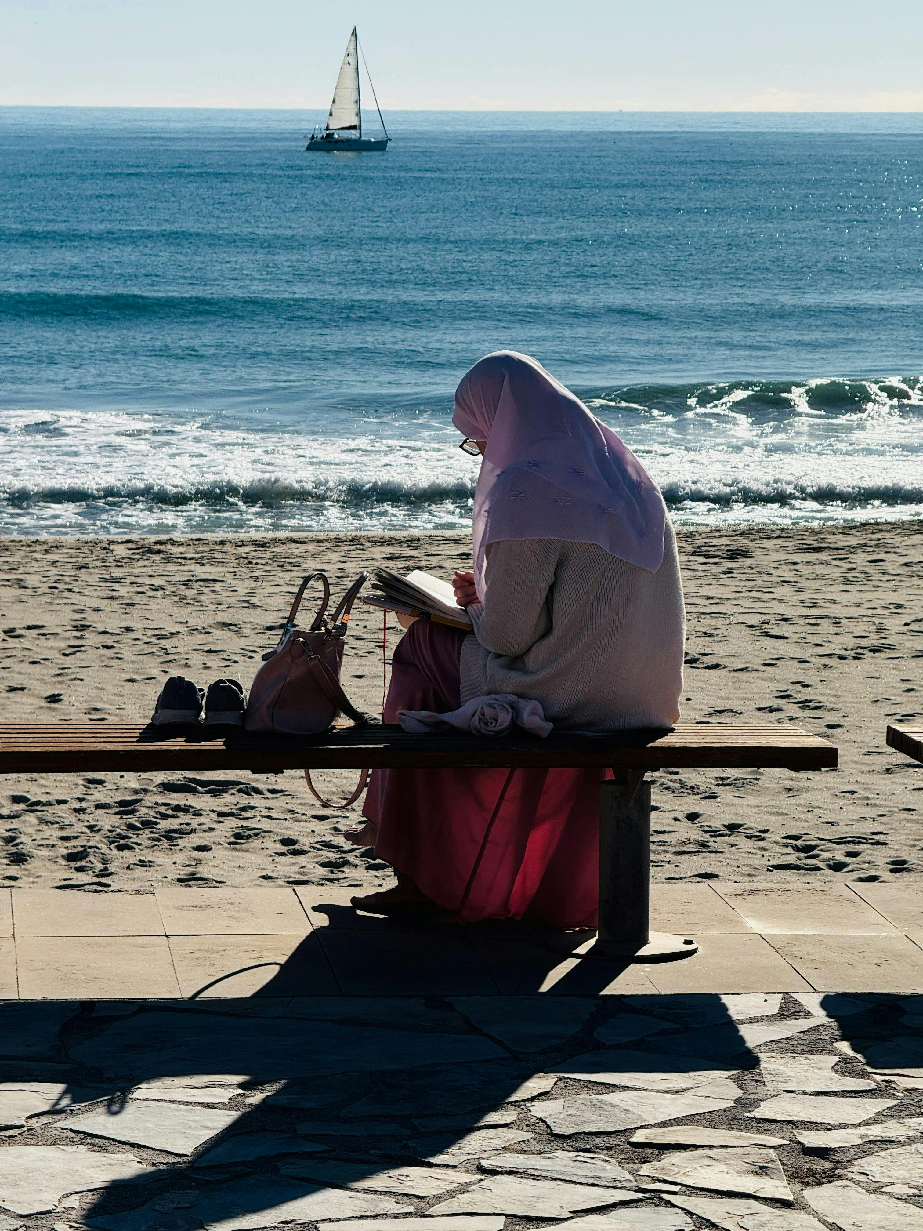 Kostnadsfria Fridfull strandscen med en kvinna som läser på en solig dag med havsutsikt. Stock foto