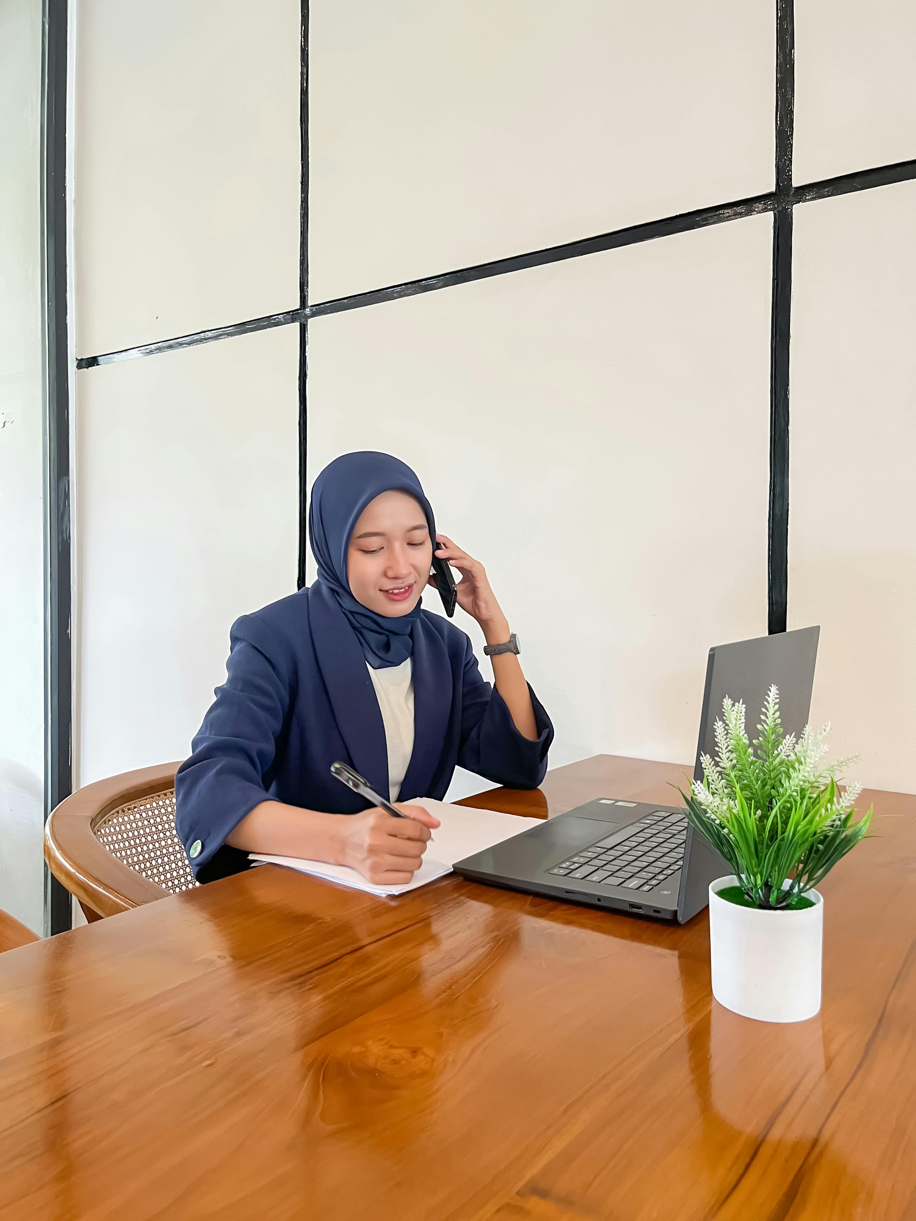 Gratis En profesjonell kvinne i hijab jobber med en bærbar PC og telefon på en koselig kafé. Arkivbilde