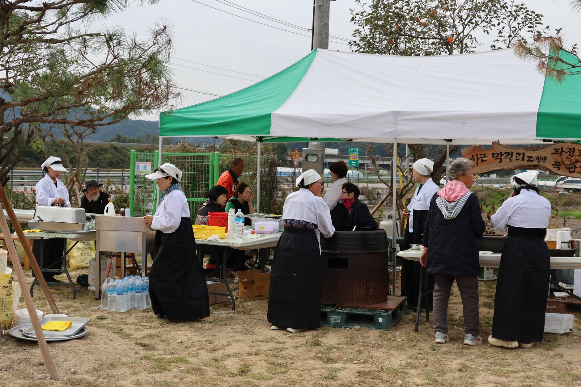 Korean outdoor market stall with people in traditional attire preparing food.
