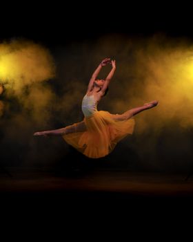 Graceful ballet dancer performs an elegant leap in a misty studio setting.