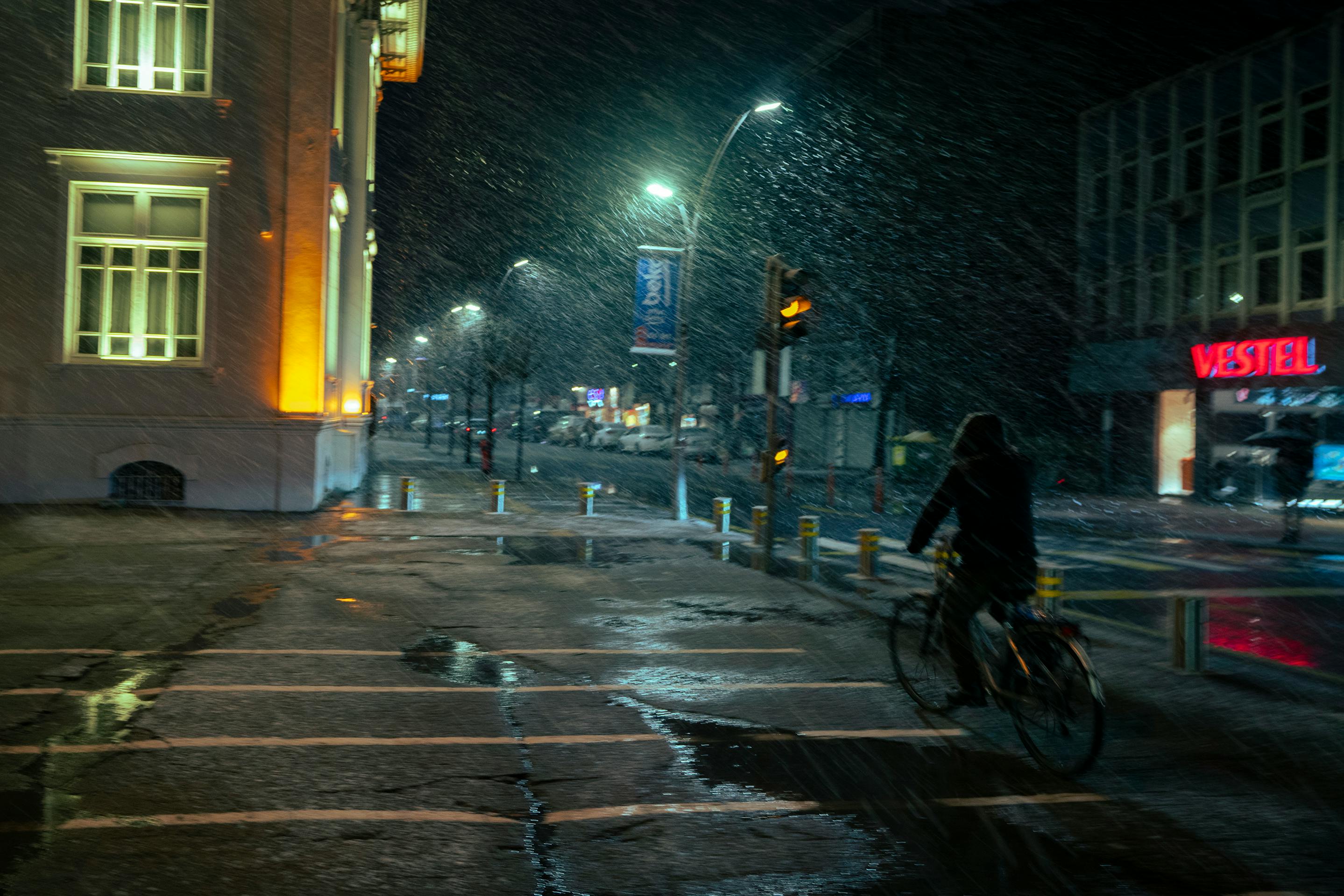 Zadarmo Cyklista sa v noci preháňa zasneženou mestskou ulicou, na ktorej svietia neónové nápisy. Fotka z fotobanky