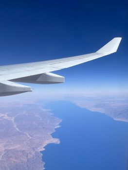A breathtaking aerial view from an airplane showing the coastline and deep blue sea under a clear sky.