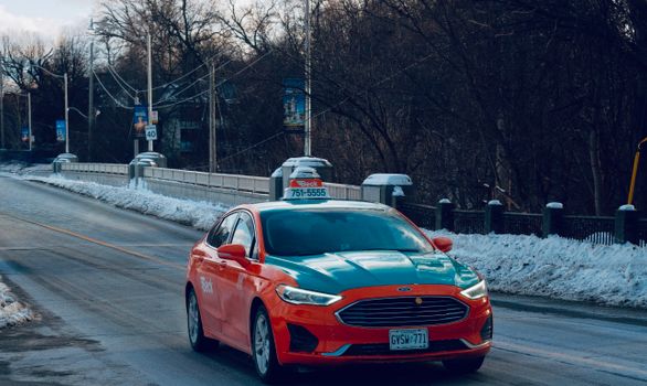 Taxi with distinct livery driving on a snowy bridge in Toronto, capturing the essence of winter travel.