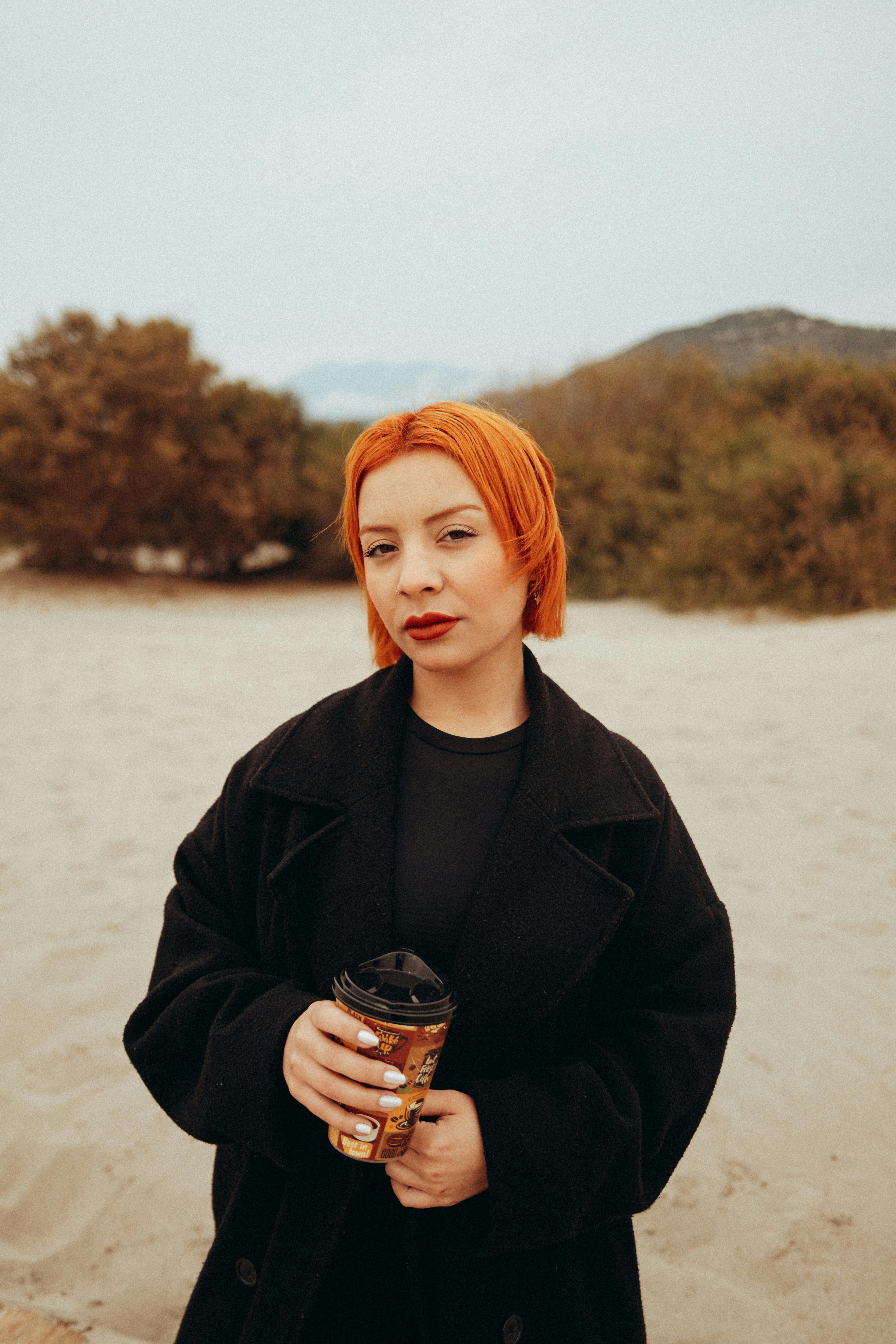 免费 一位年轻女子手捧咖啡杯，站在沙质户外环境中。 素材图片