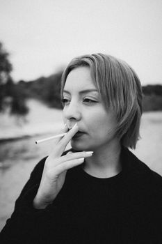 Thoughtful woman smoking in a black and white outdoor portrait.