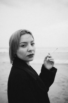 Black and white portrait of a woman smoking by the sea, evoking a moody, contemplative atmosphere.