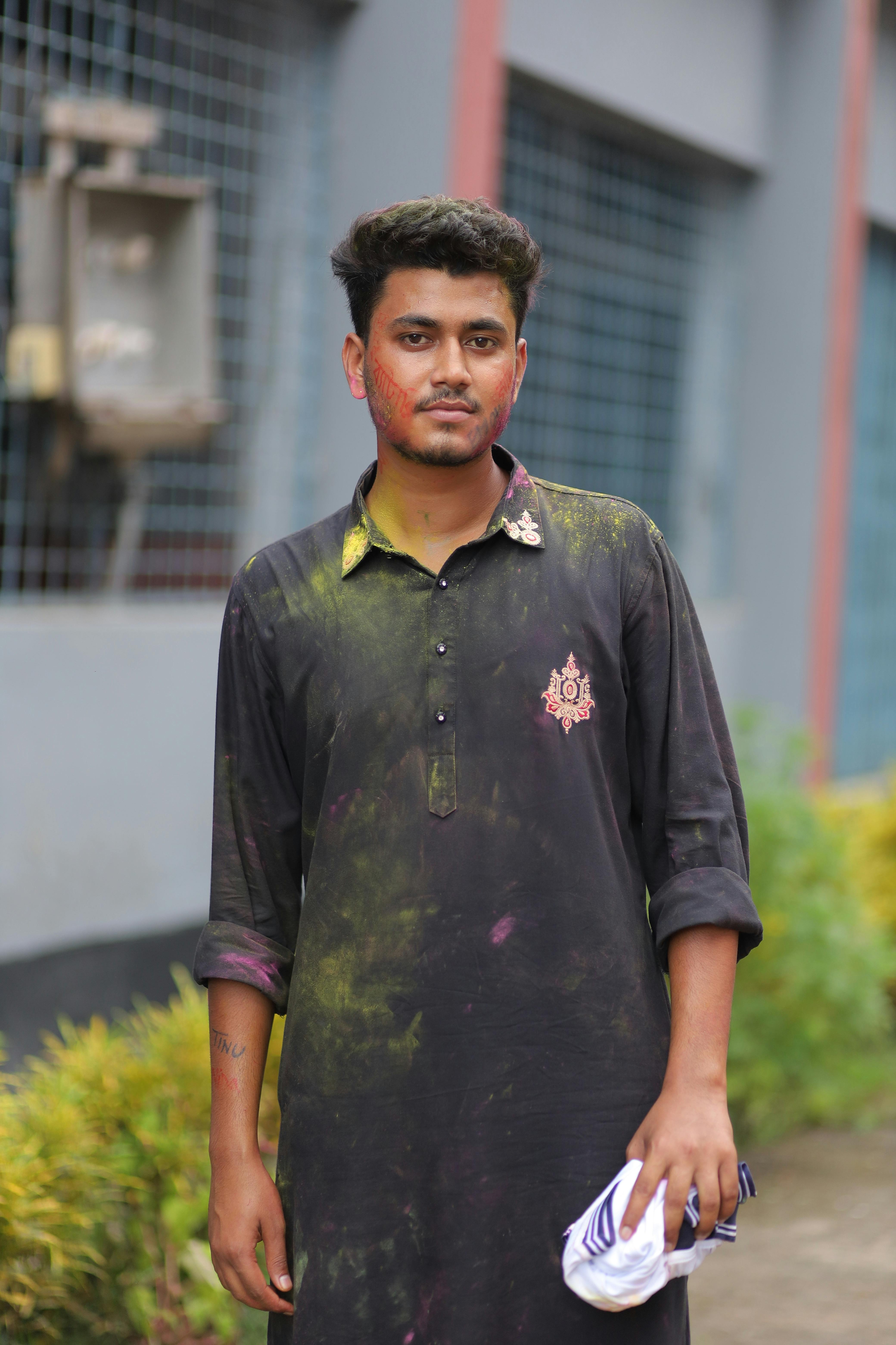 Young man in Patuakhali celebrating festival with colorful powder on traditional attire.