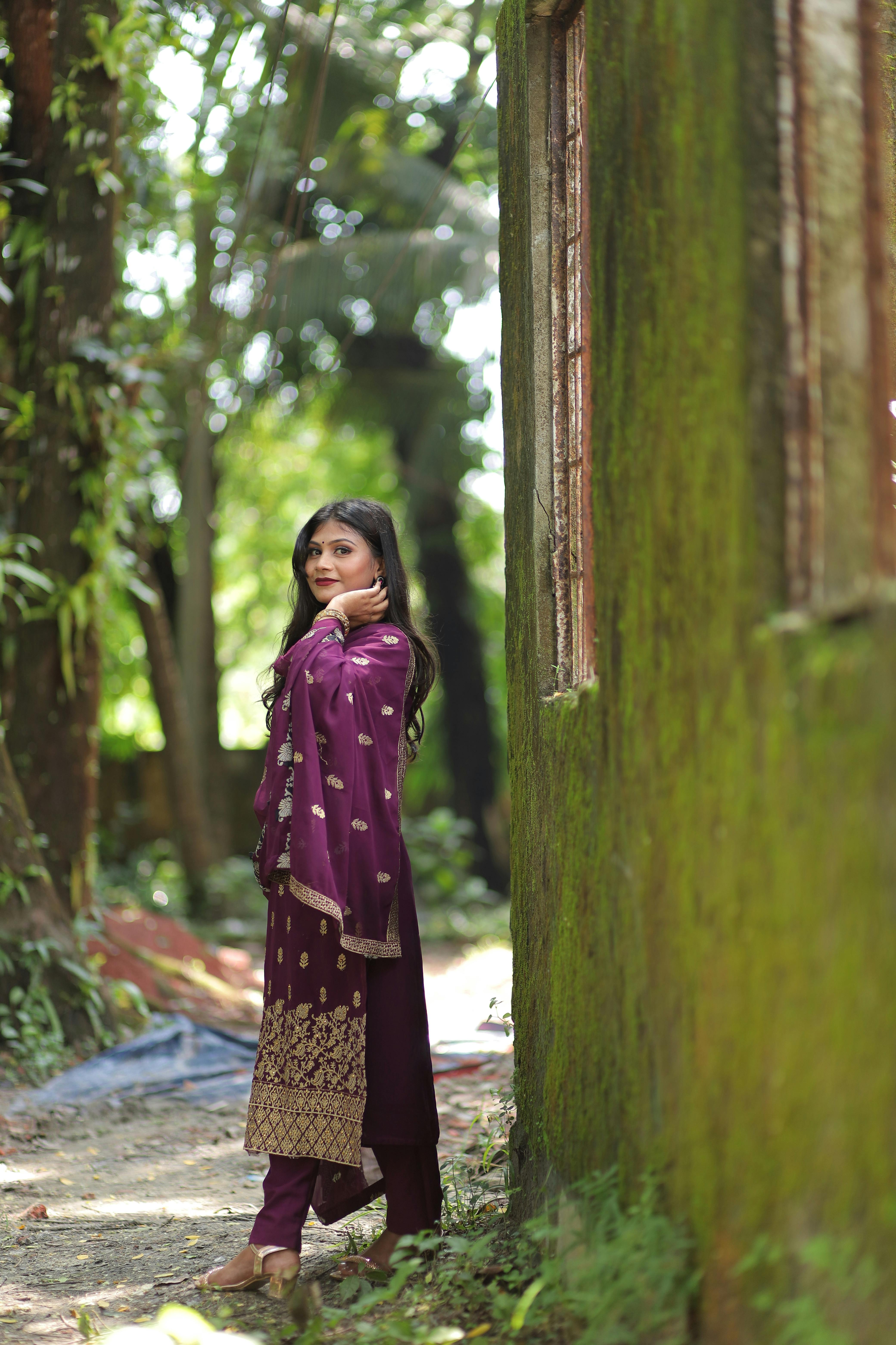 gratis Elegant portret van een vrouw in een traditionele magenta jurk in een weelderige buitenomgeving. Stockfoto