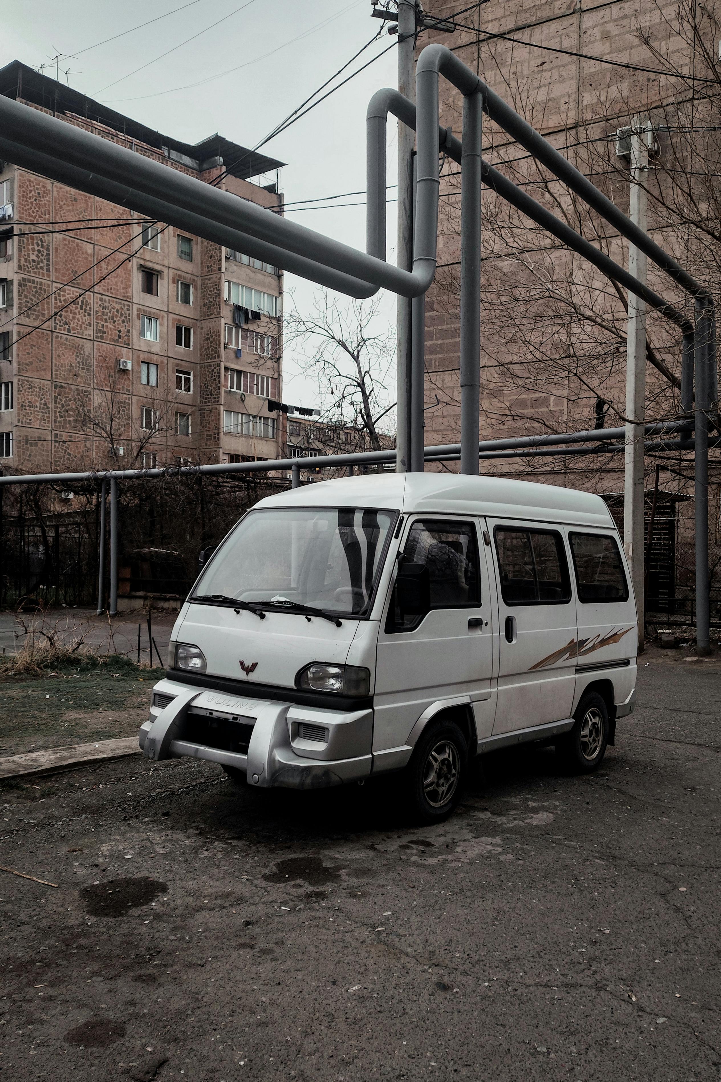 免費 白色廂型車停在城區，背景是工業管道和建築物。 圖庫相片