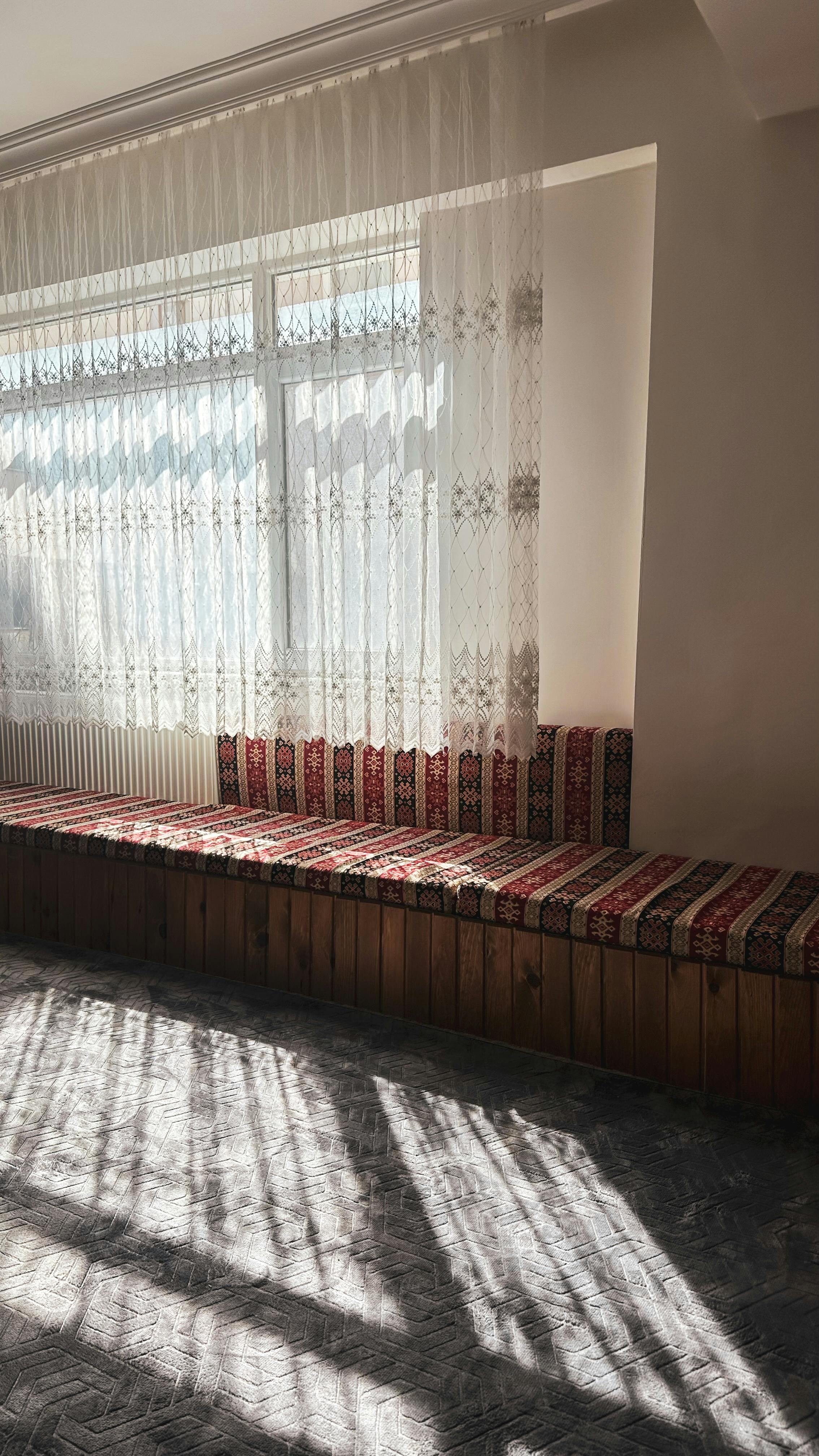 Sunlit room in Bolu, Türkiye, featuring traditional Turkish seating with patterned cushions and lace curtains.