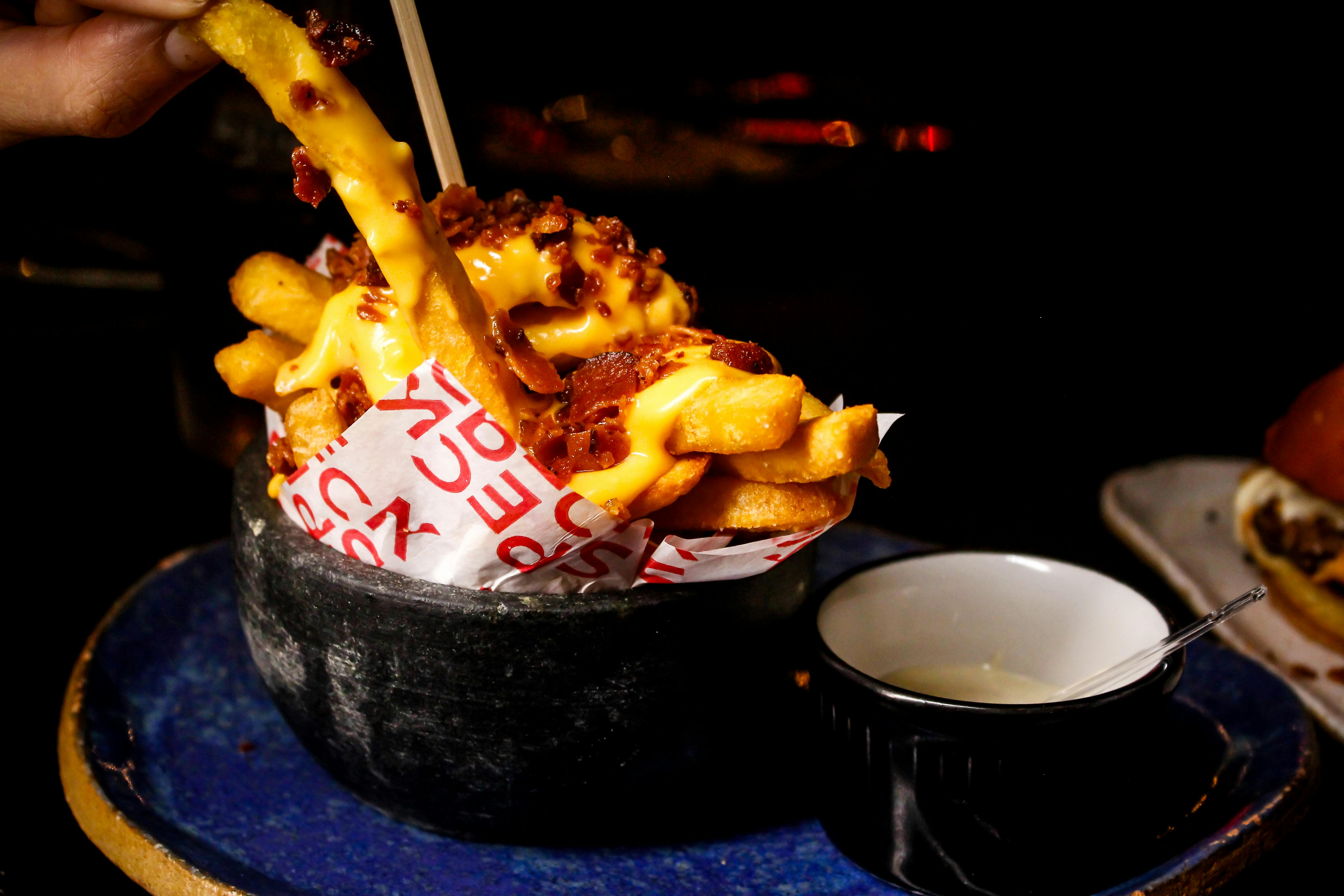 De franc Delicioses patates fregides amb formatge i bacó servides amb salsa en un ambient fosc. Foto d'estoc