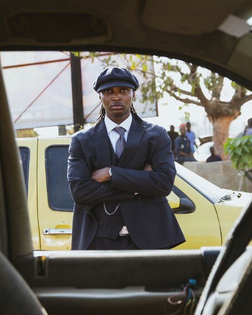 Free A stylish man in a suit and cap stands confidently by a yellow taxi in an urban setting. Stock Photo