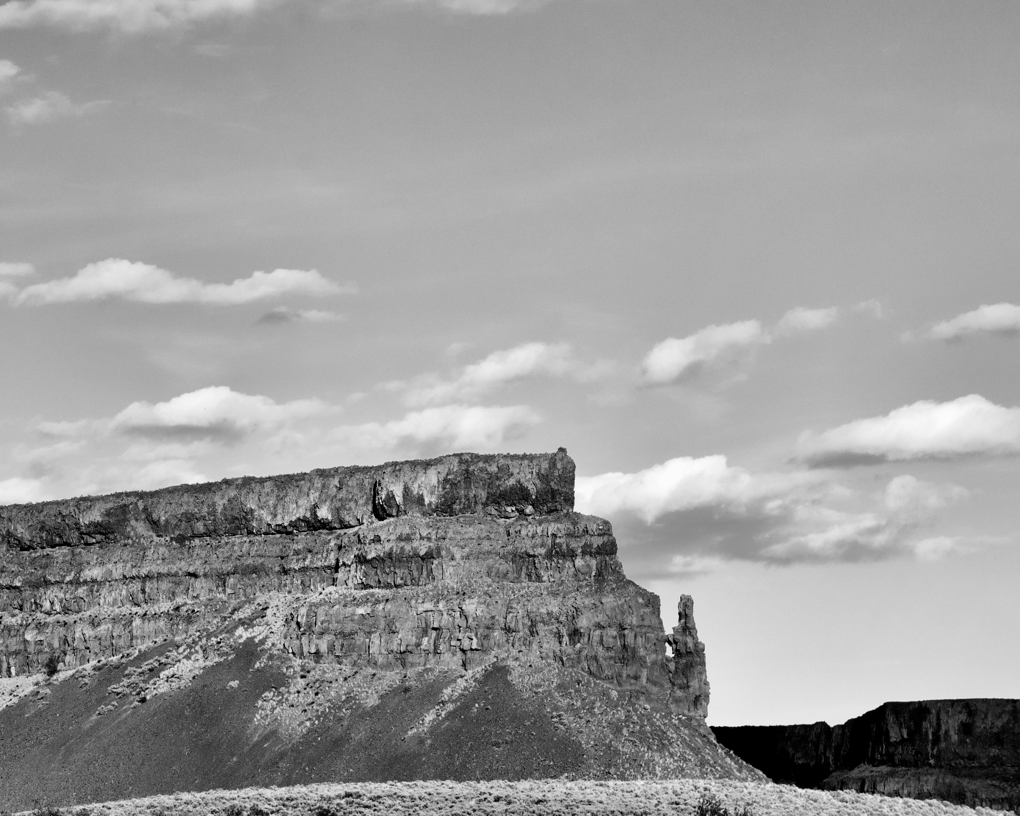 Kostnadsfria Fantastiskt svartvitt foto som visar en dramatisk ökenklippa under en molnig himmel. Stock foto