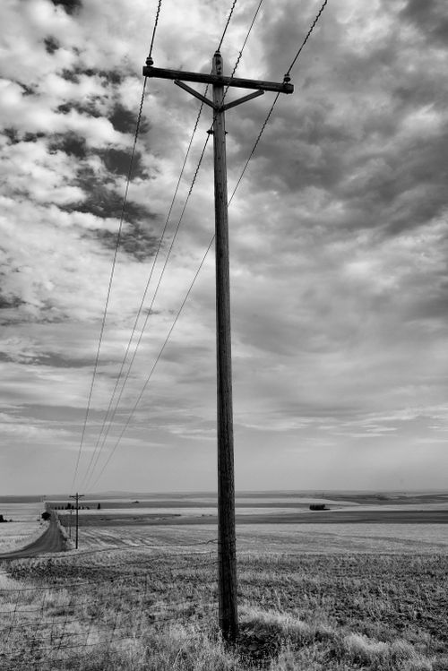 Free Lonely telephone pole in a vast rural landscape with dramatic skies, captured in black and white. Stock Photo