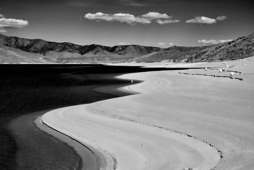 Black and white photo of a tranquil landscape featuring curved sandbanks and a placid lake.