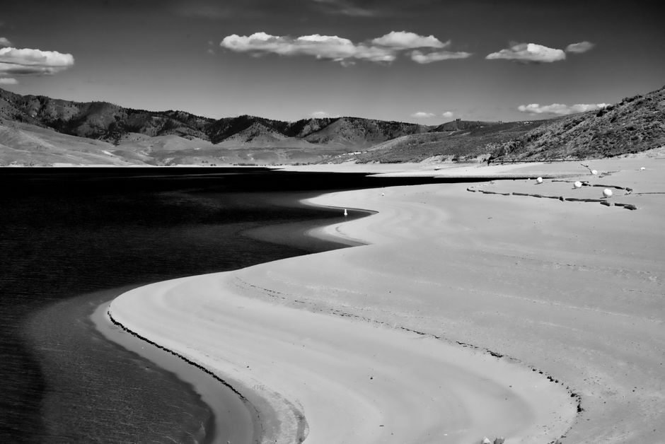 Black and white photo of a tranquil landscape featuring curved sandbanks and a placid lake.
