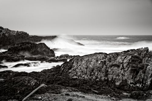 Free A dramatic black and white photo showcasing rugged rocky coastline with crashing waves. Stock Photo