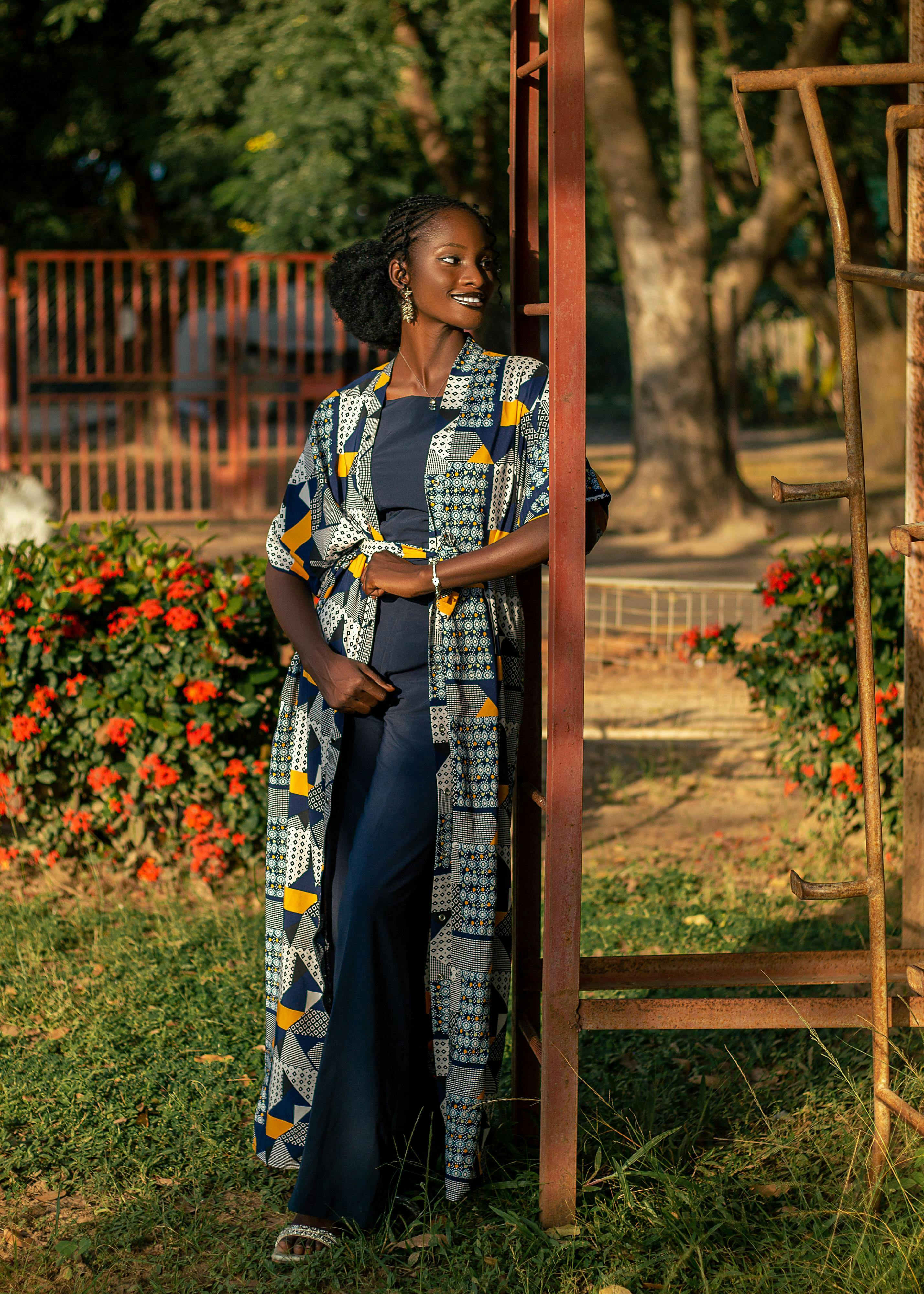 Gratuit Une femme se tient élégamment à l'extérieur, vêtue d'une robe imprimée aux couleurs vives, profitant d'une journée ensoleillée. Photos