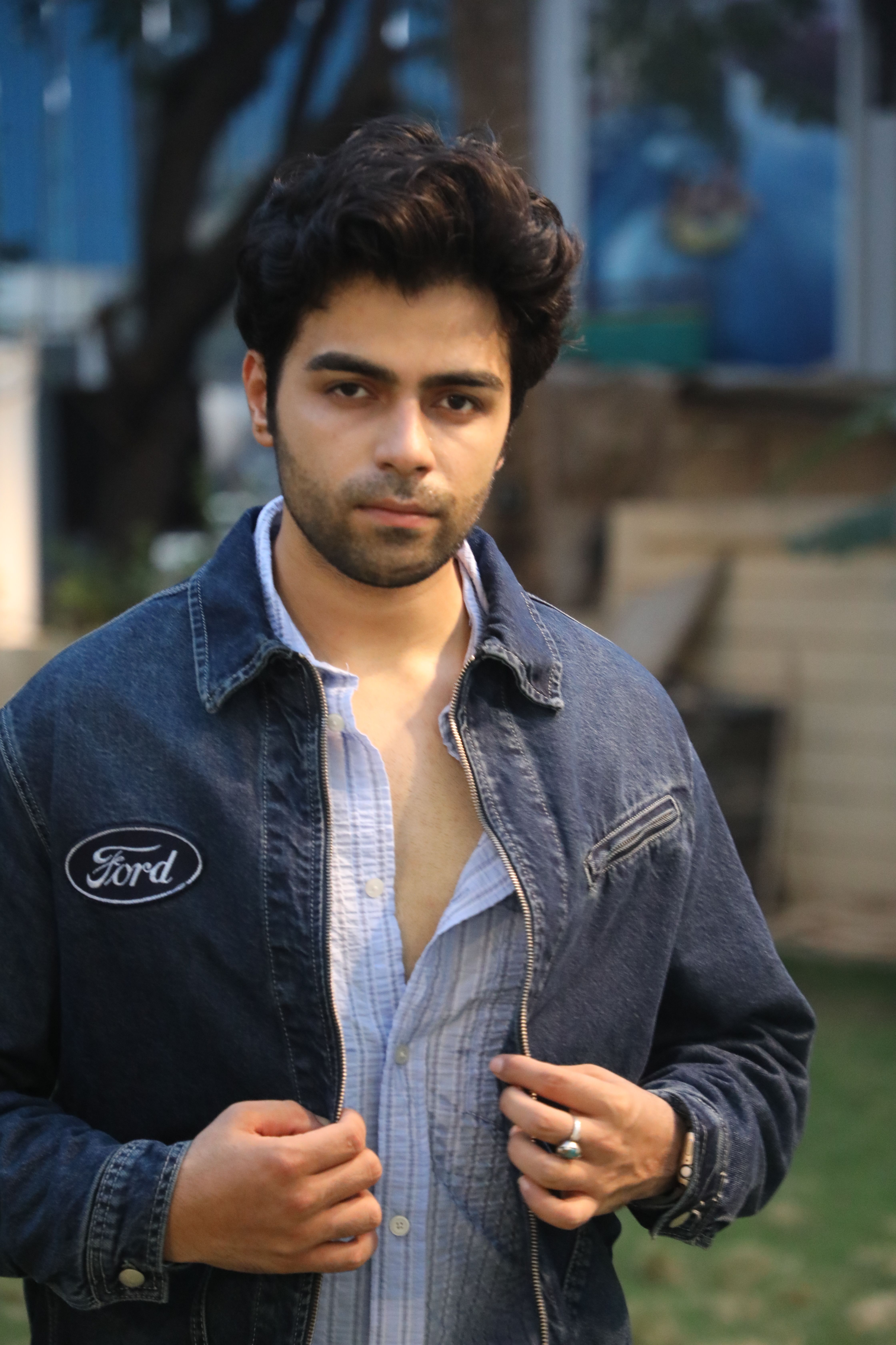 A young man poses outdoors in a denim jacket, exuding confidence and style.