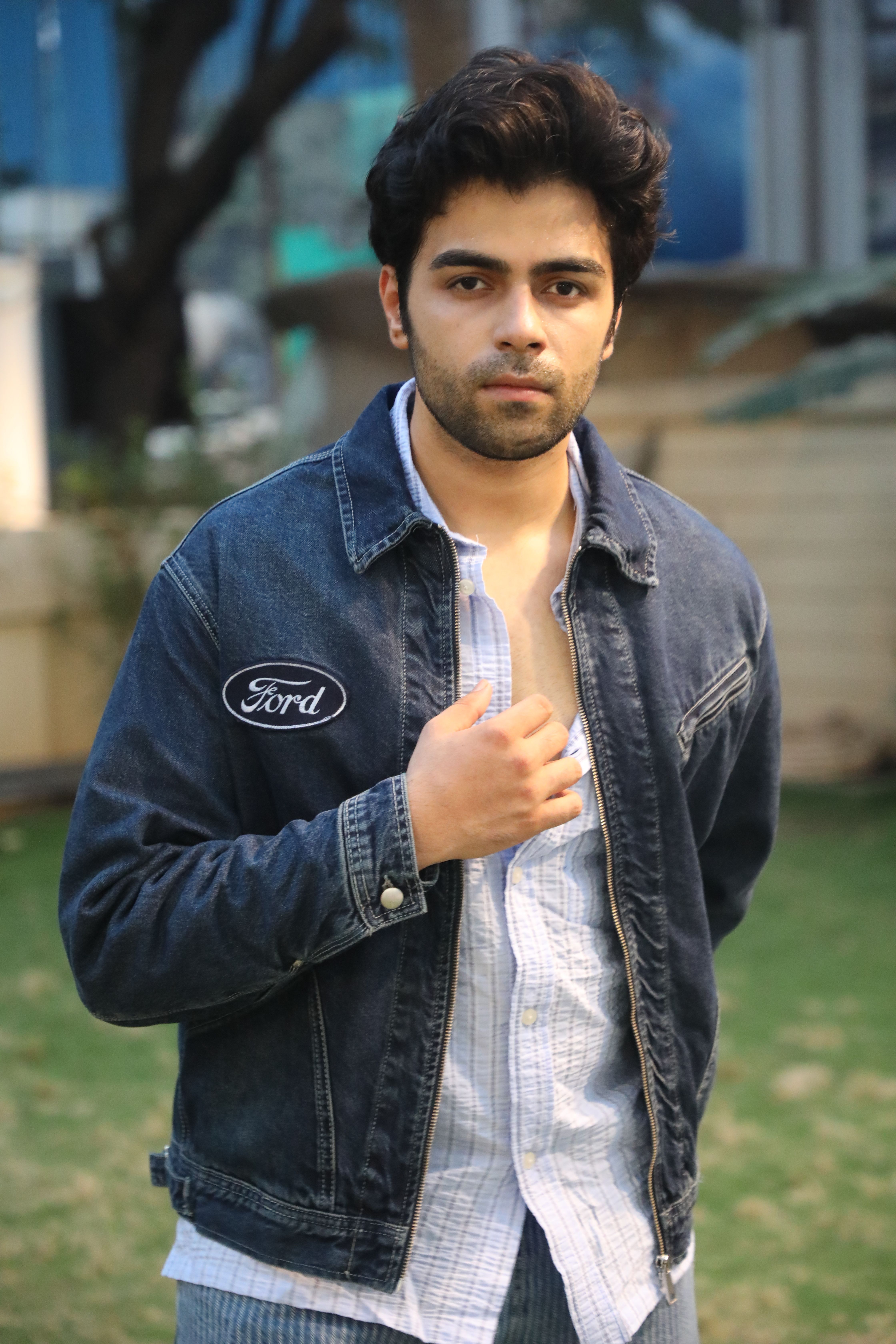 Young man outdoors wearing a denim jacket on a sunny day.