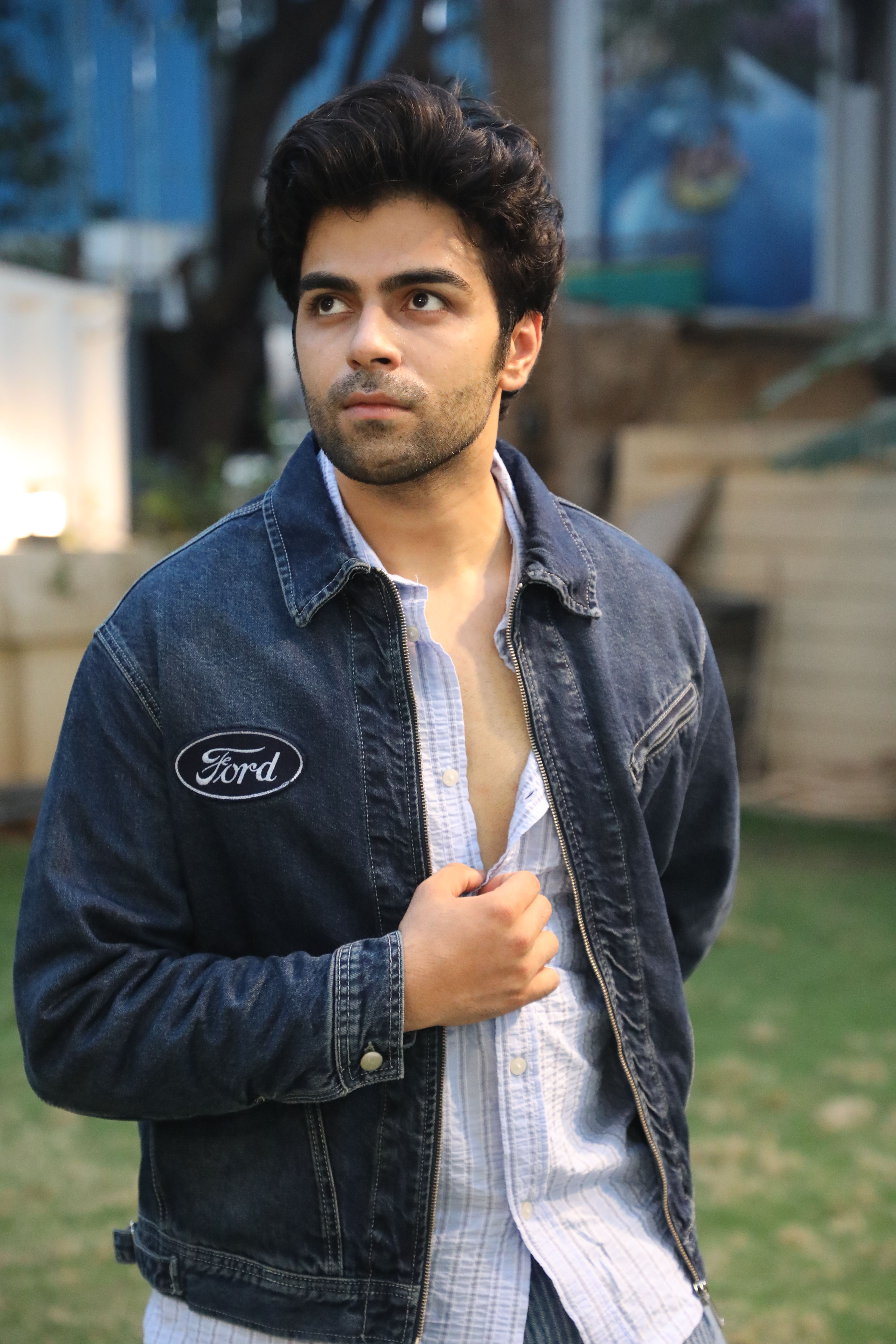 Young man wearing a denim jacket standing outdoors on a sunny day.