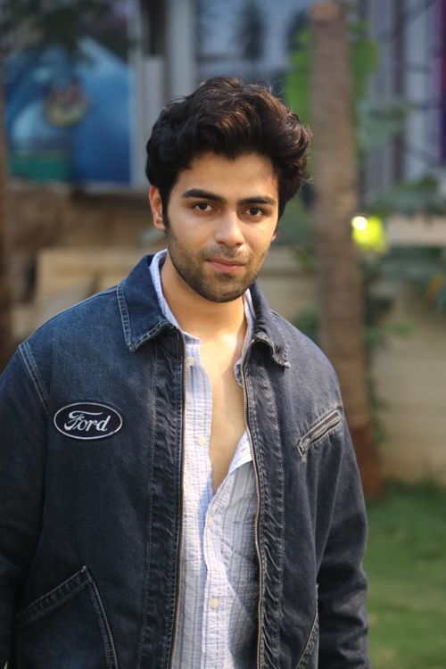 Free Casual portrait of a young man in a denim jacket, outdoors in a garden-like setting. Stock Photo