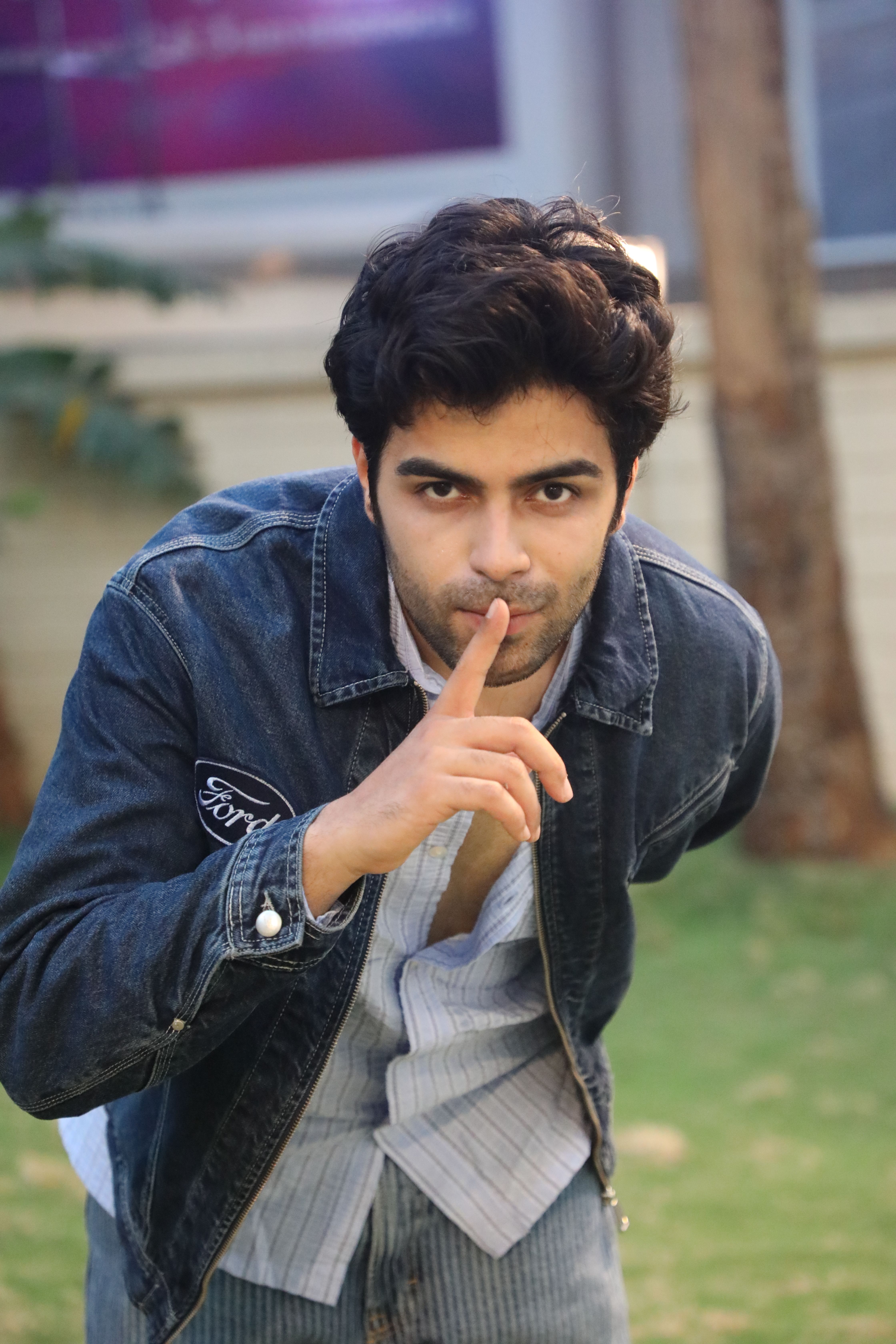 A man in casual attire outside making a shushing gesture, suggesting quiet or secrecy.