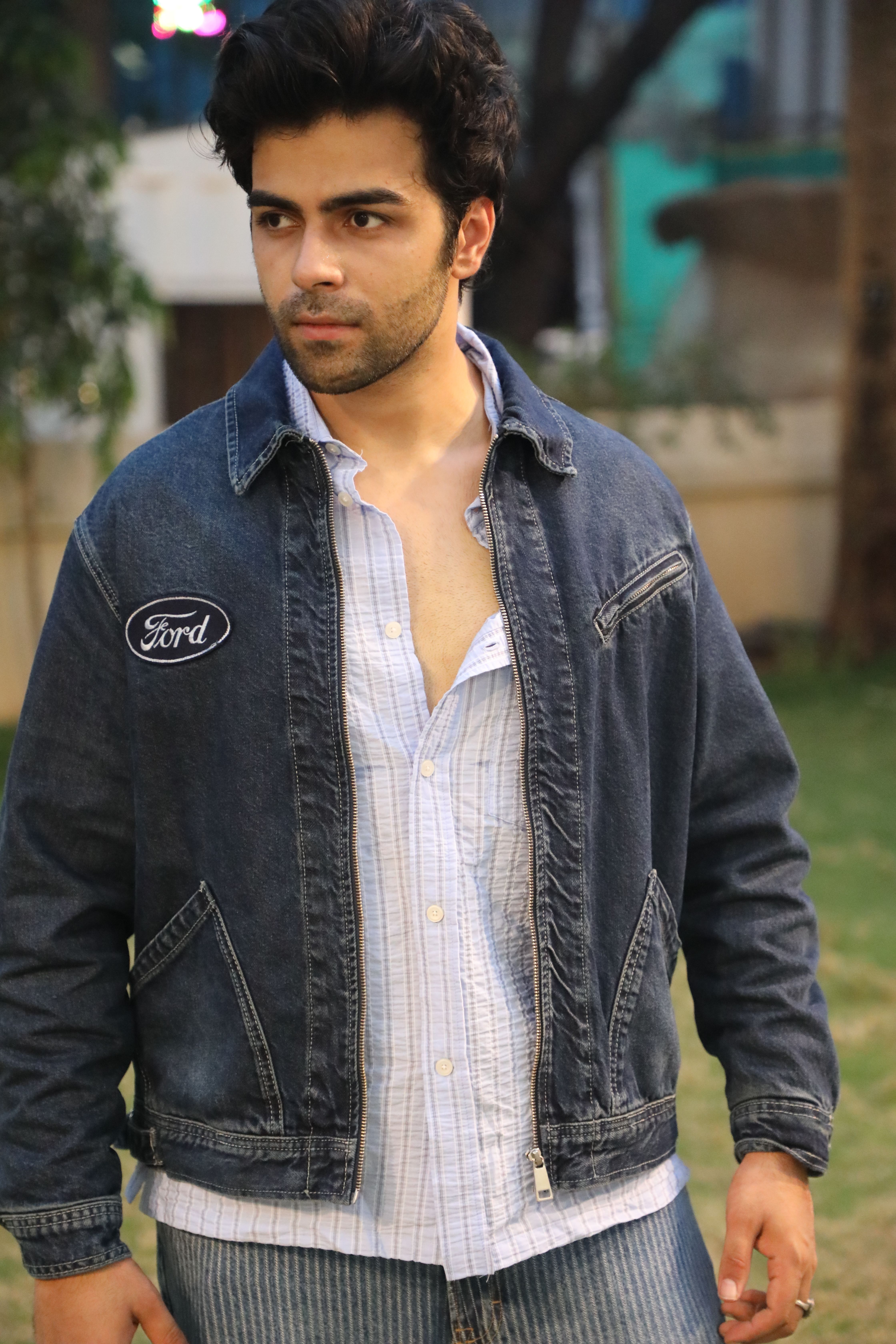 Young man in denim jacket poses outdoors, showcasing casual style.